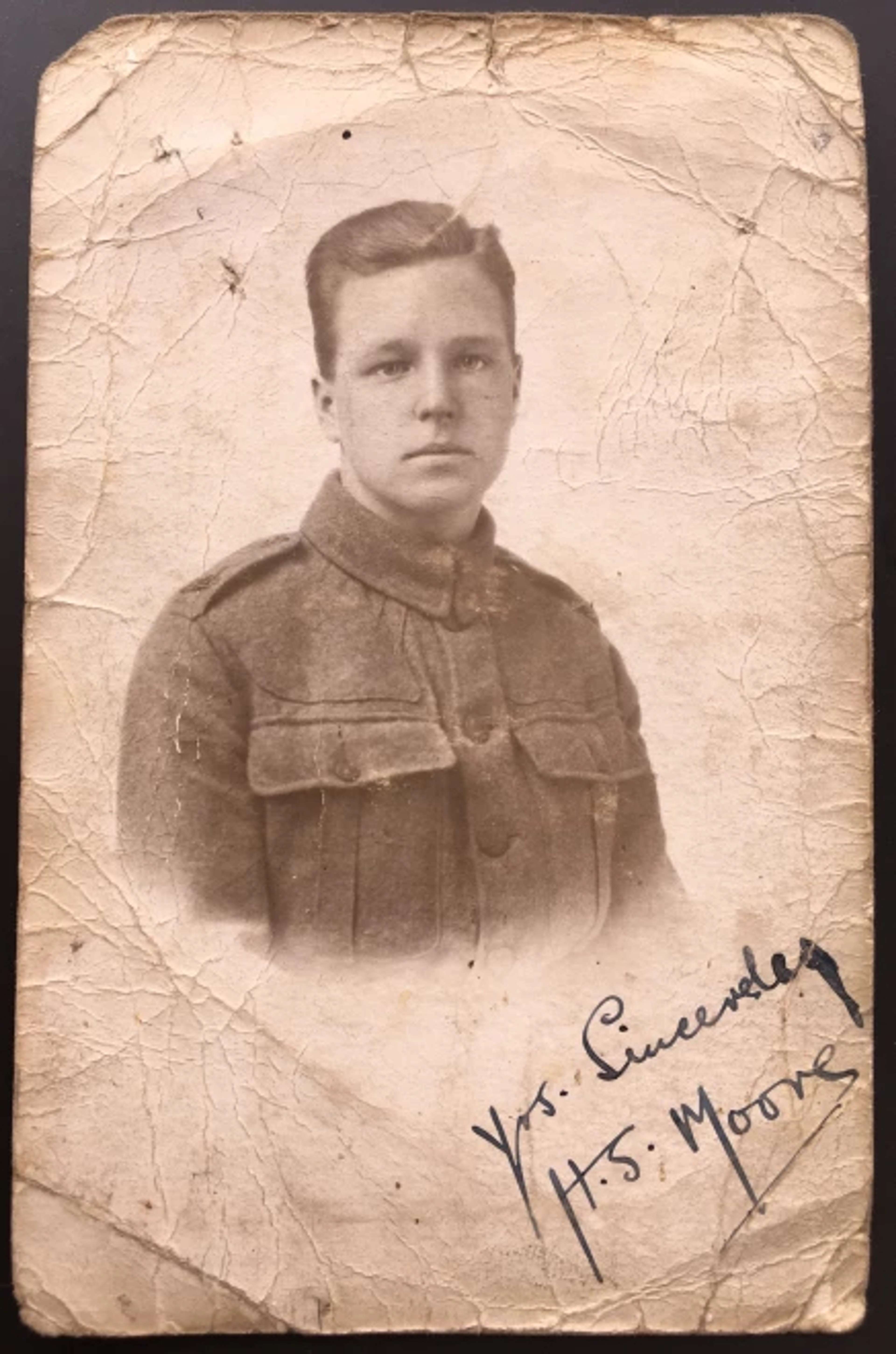 Une vignette représentant un jeune homme en uniforme militaire sur un papier froissé. Le jeune homme, identifié comme Henry Moore, avec des cheveux peignés sur le côté et une expression faciale stoïque, est représenté dans le cadrage circulaire. Dans le coin inférieur droit, la vignette est signée des initiales « H.S. Moore ».