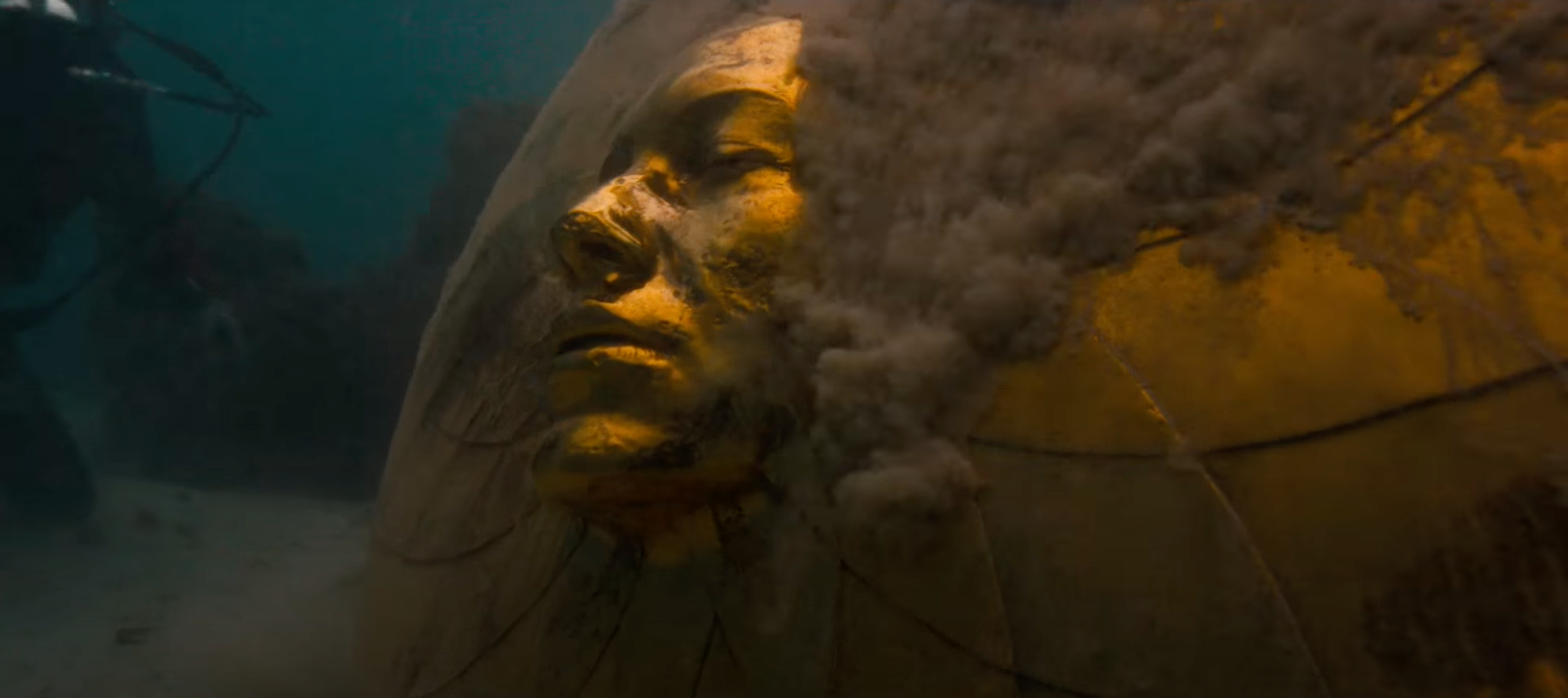 Une sculpture dorée de grande taille représentant un visage est visible sous l'eau, entourée de sable.