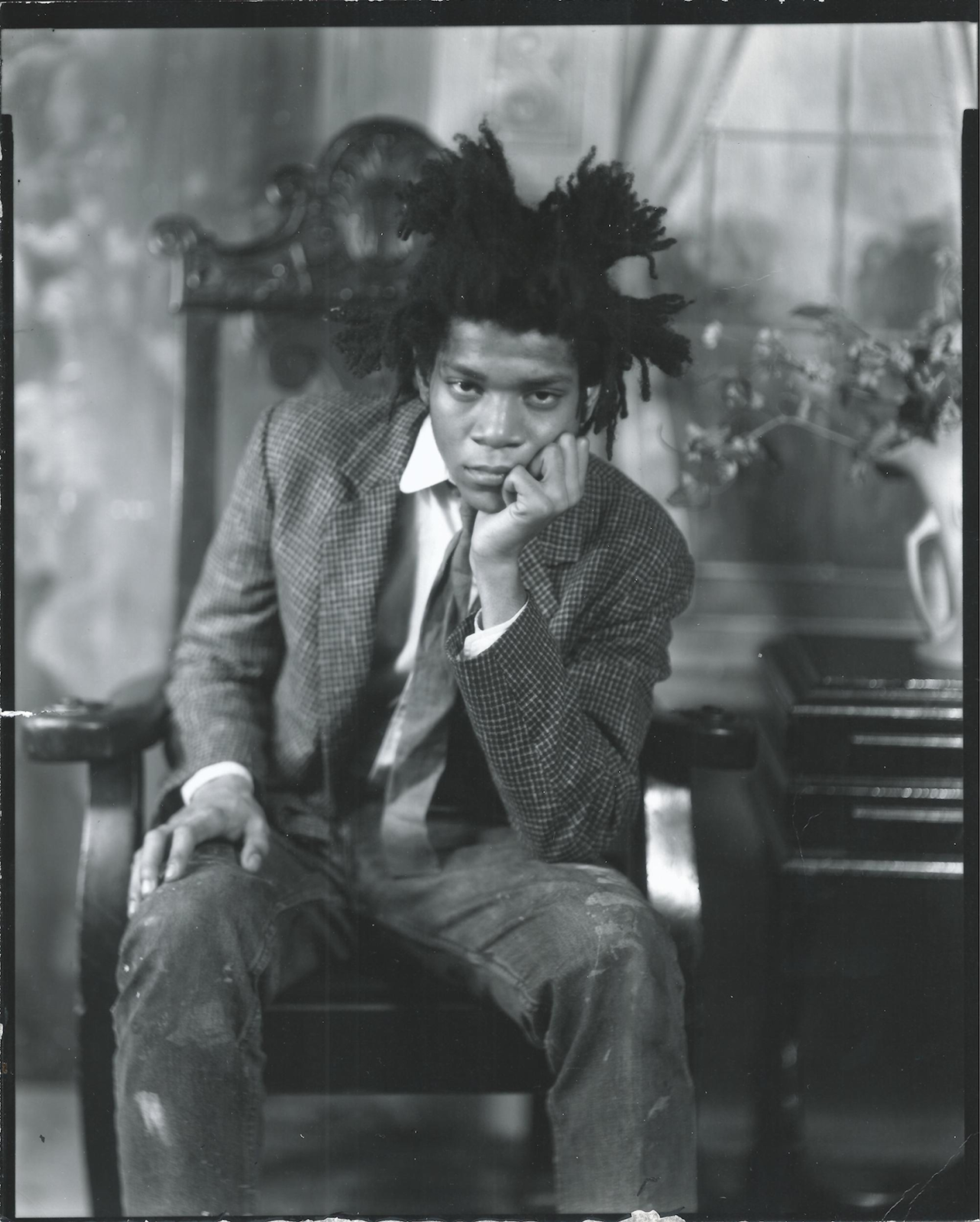 Photographie en noir et blanc de Jean-Michel Basquiat assis sur une chaise.