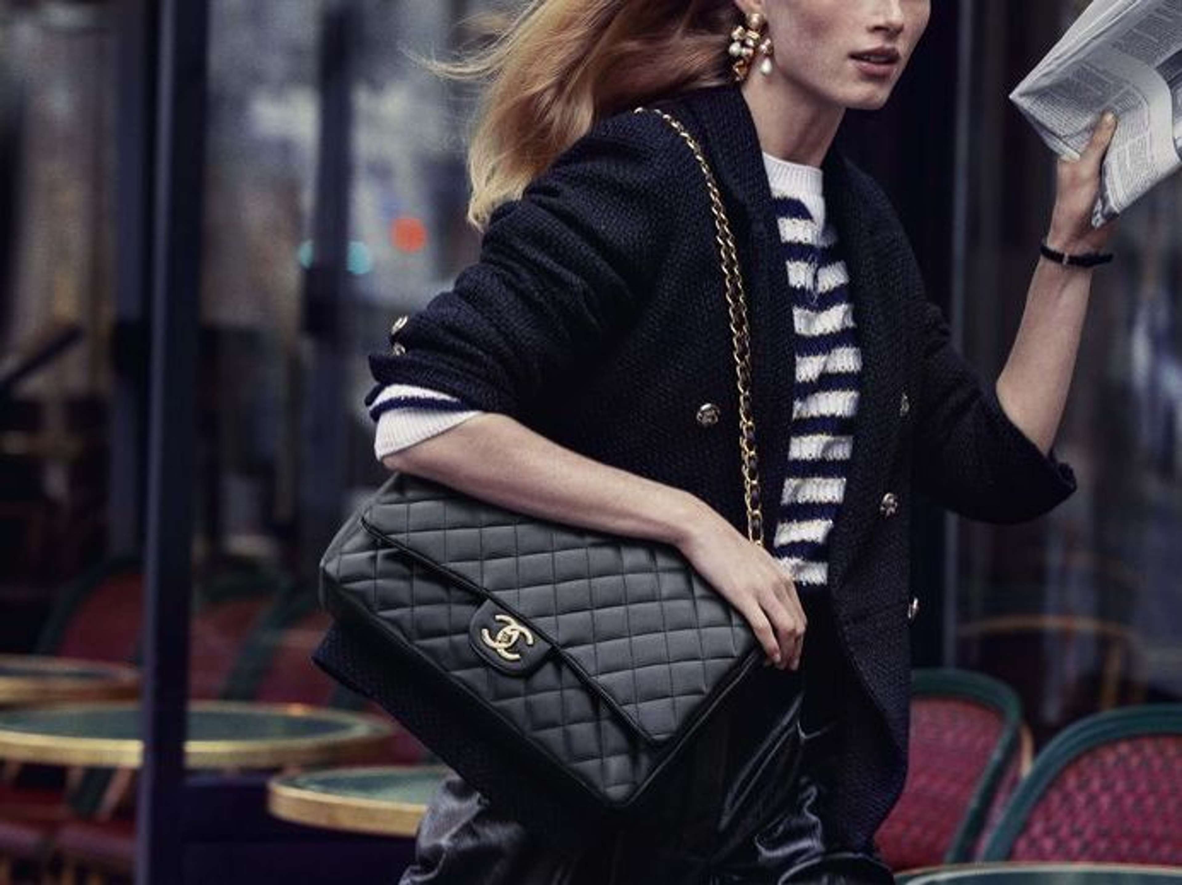 Une photo d'un mannequin, vêtu(e) d'un haut rayé et d'un cardigan, tenant un grand sac Chanel Classic Flap Bag noir.