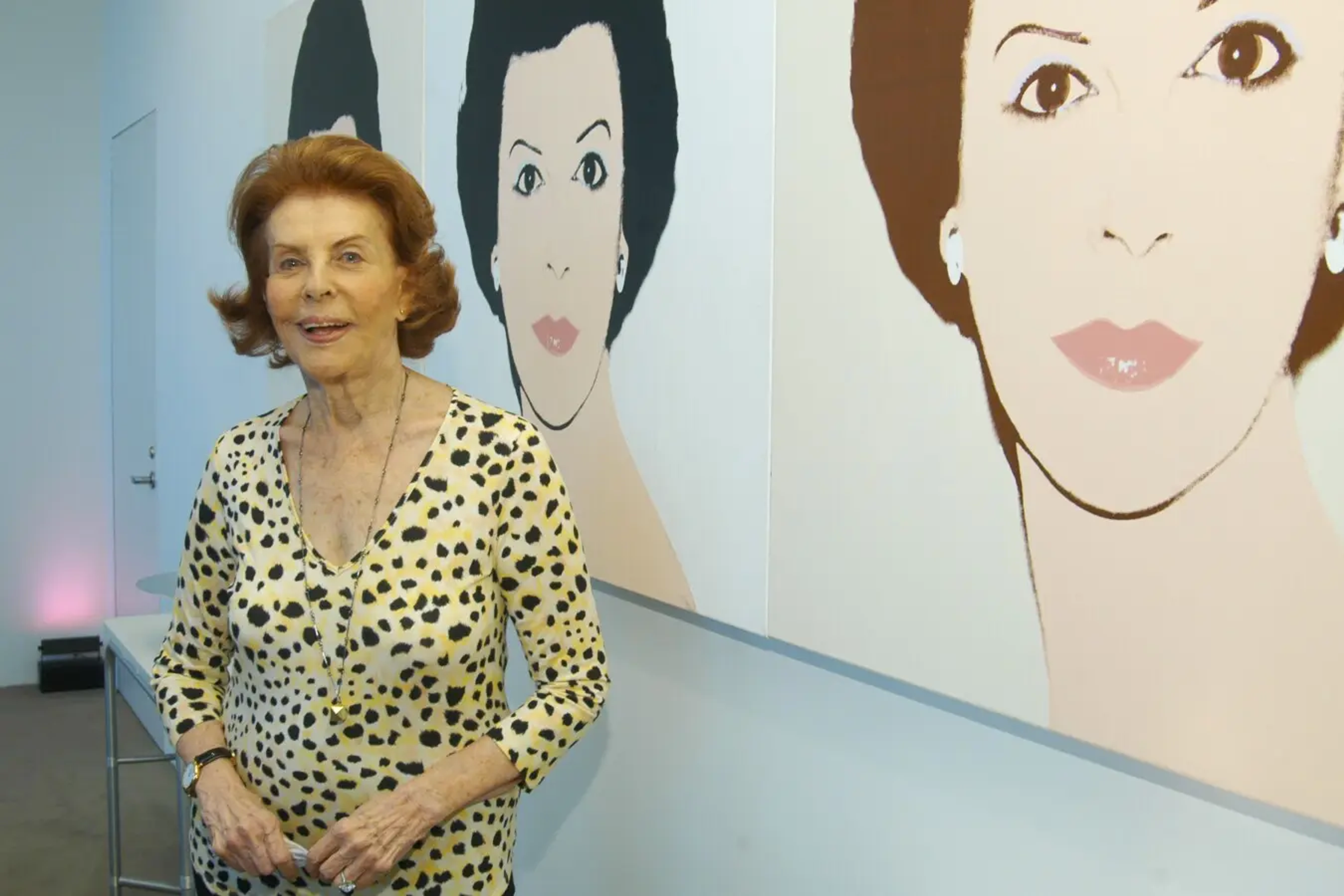 Cette photographie montre Emily Fisher Landau devant une série de portraits réalisés d'elle par Andy Warhol.