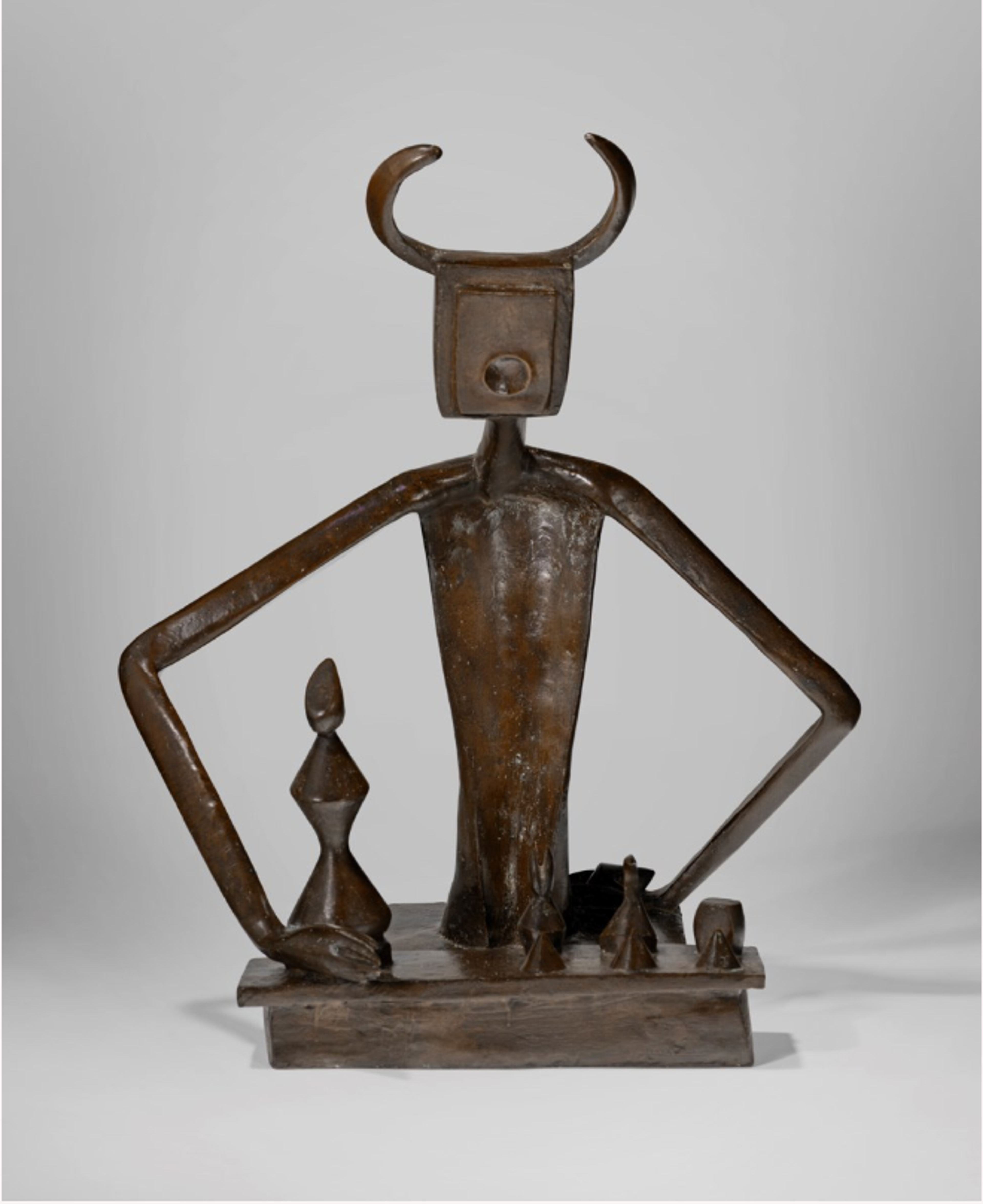 A bronze sculpture of a stylised humanoid ‘King’ figure with angular arms akimbo and a rectangular head topped with curved horn-like shapes. The figure stands on a rectangular base, accompanied by a smaller ‘Queen’ chess piece and other abstract geometric pieces.