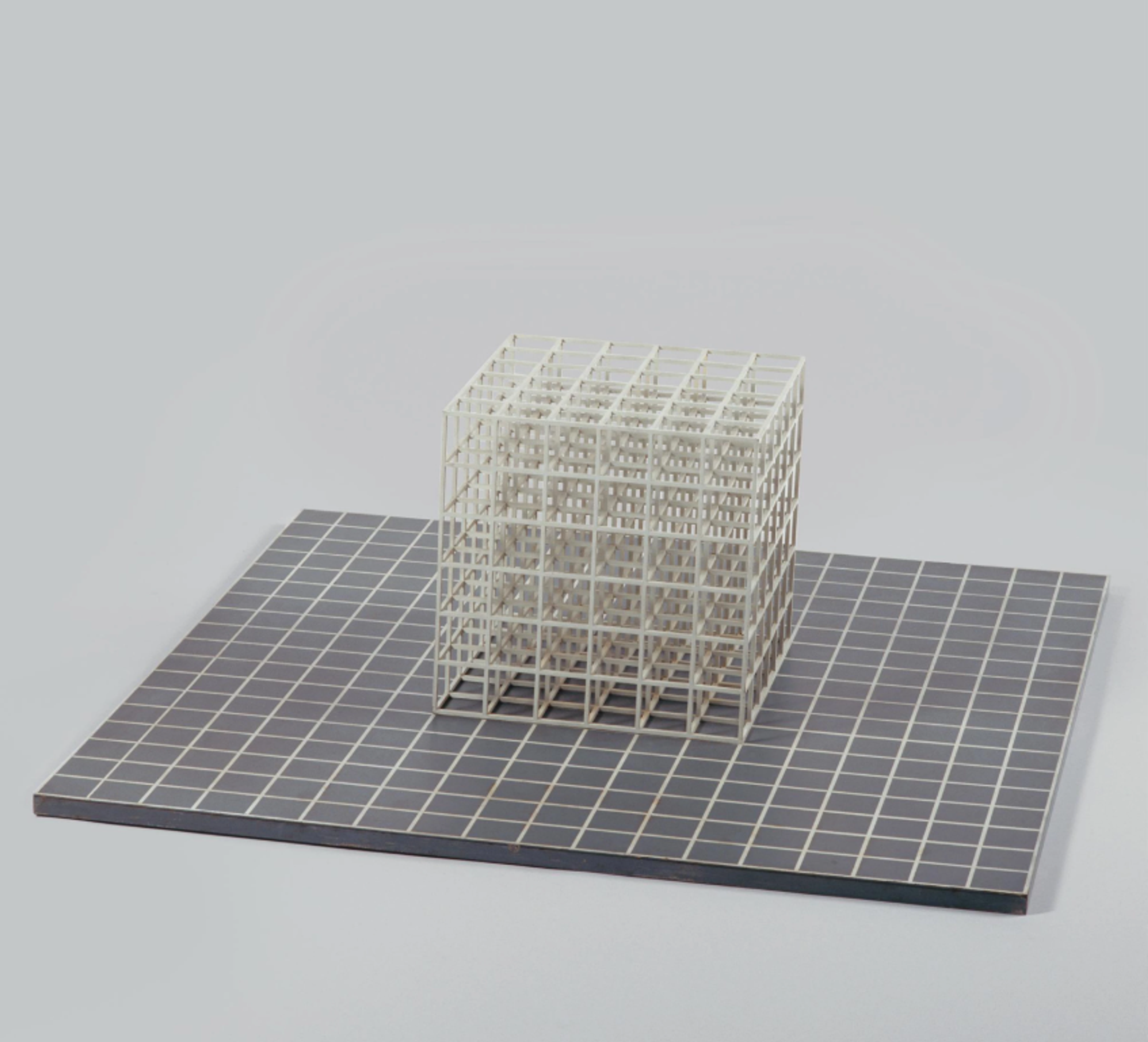A geometric arrangement of open white cubes to form a larger cube, set on a gridded grey base.