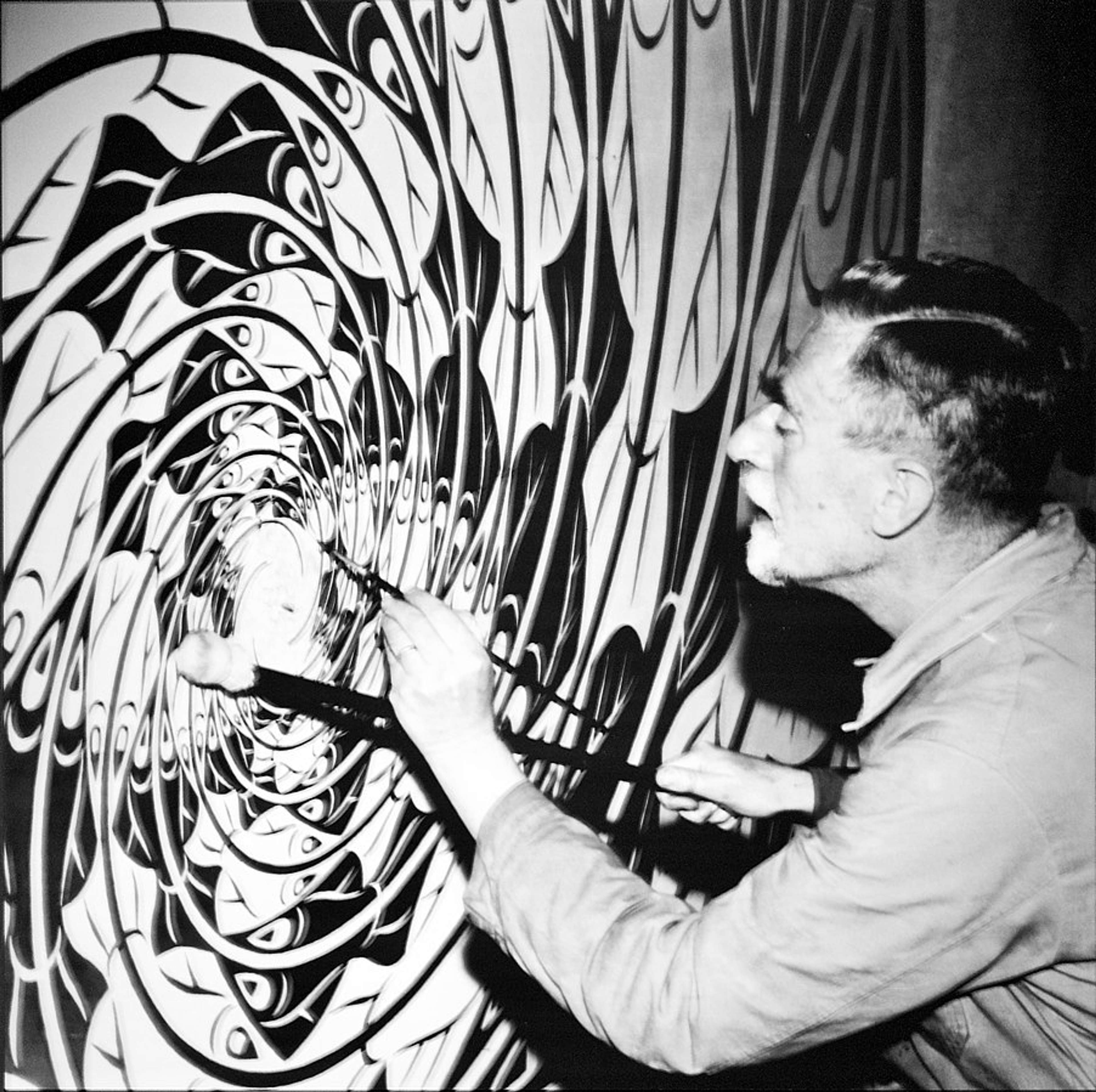 Une photographie en noir et blanc de M. C. Escher travaillant sur une peinture à motif en spirale.