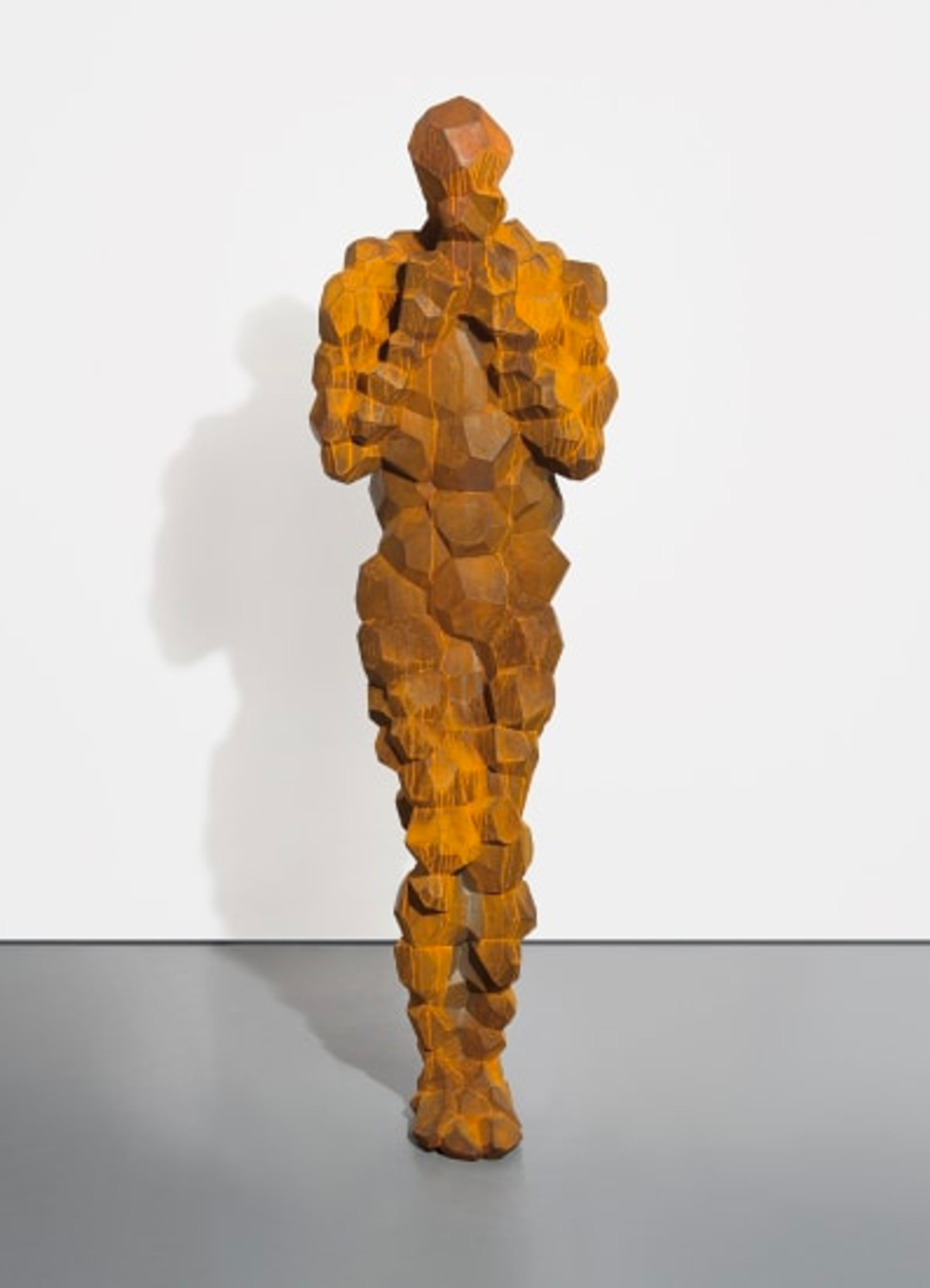 Une sculpture en fonte représentant une figure humaine debout, avec des traits corporels bien définis et une surface texturée et bulbeuse.