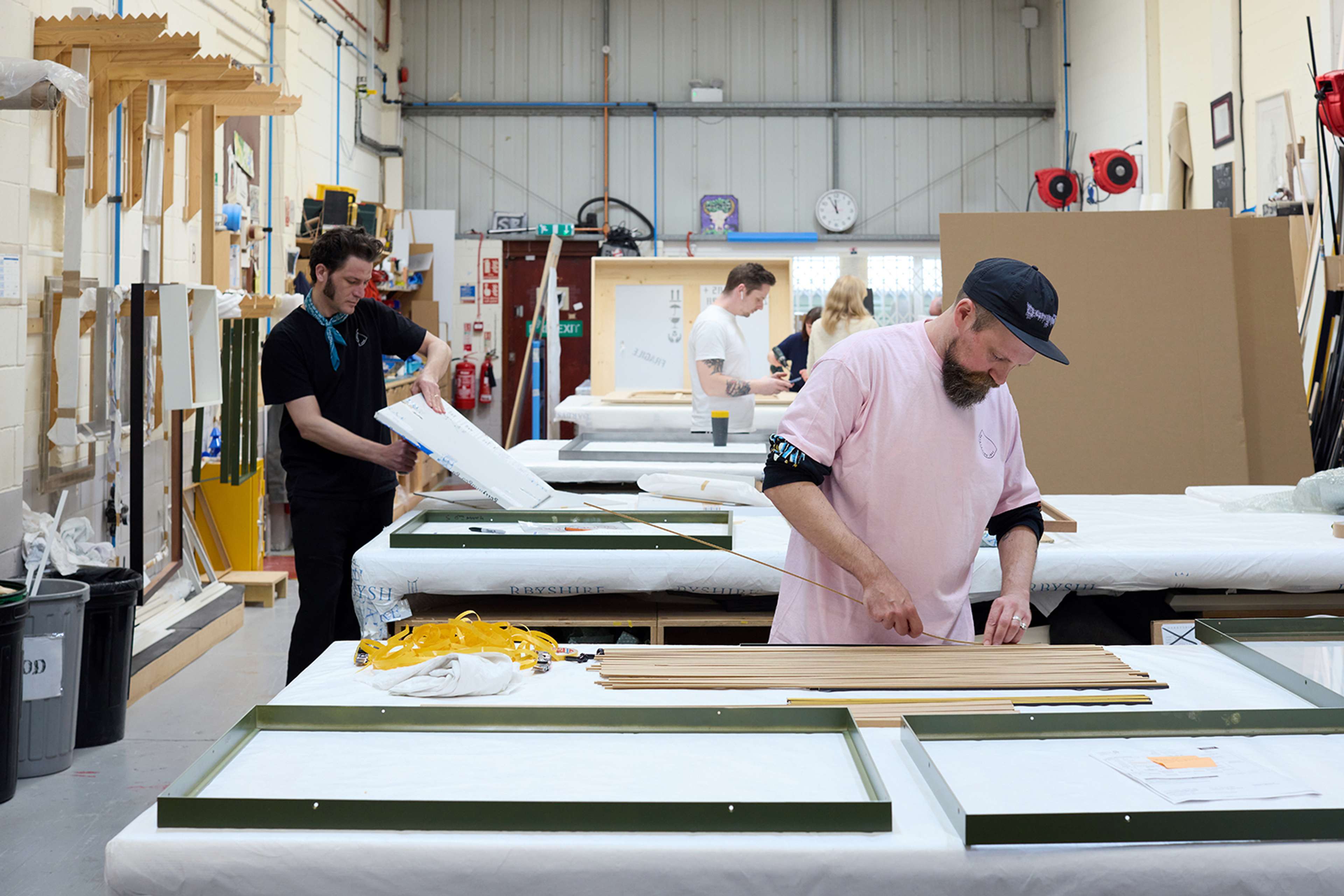 Des consultants de Darbyshire assemblent des cadres et préparent des œuvres d'art sur de grandes tables de travail dans un atelier animé.