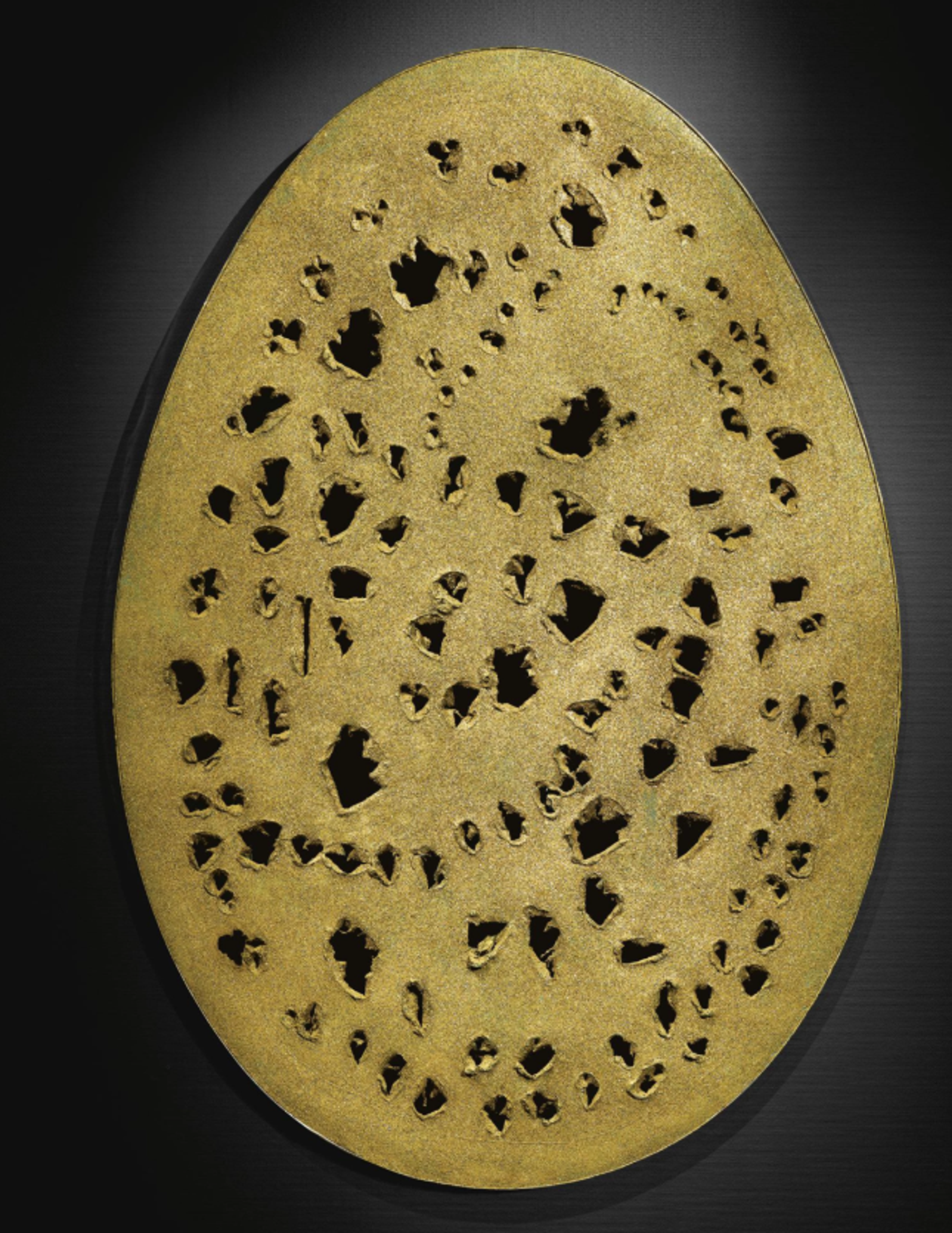 A glittery gold egg shape, covered in medium-to-large perforations, each irregular in shape and size.