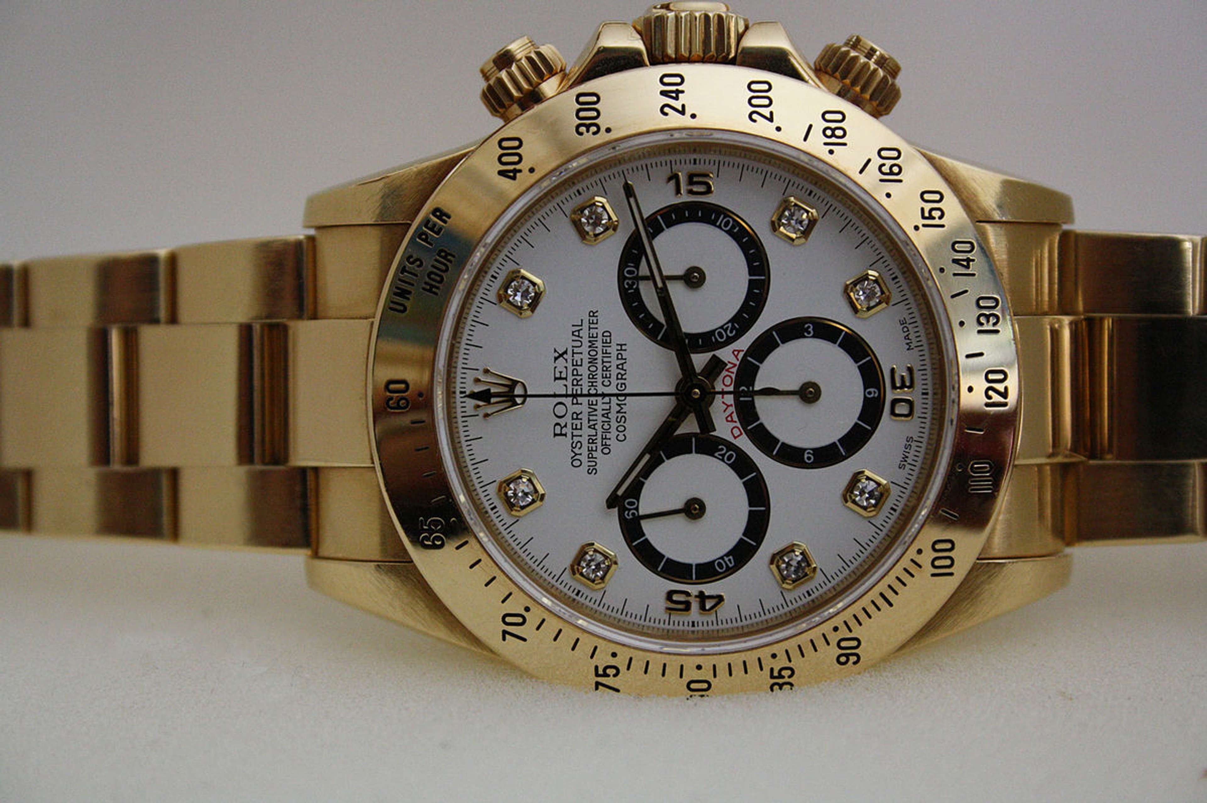 Une Rolex Daytona, lancée pour la première fois en 1963. Sur fond blanc, la montre présente un bracelet en métal doré et un cadran blanc orné de trois sous-cadrans.