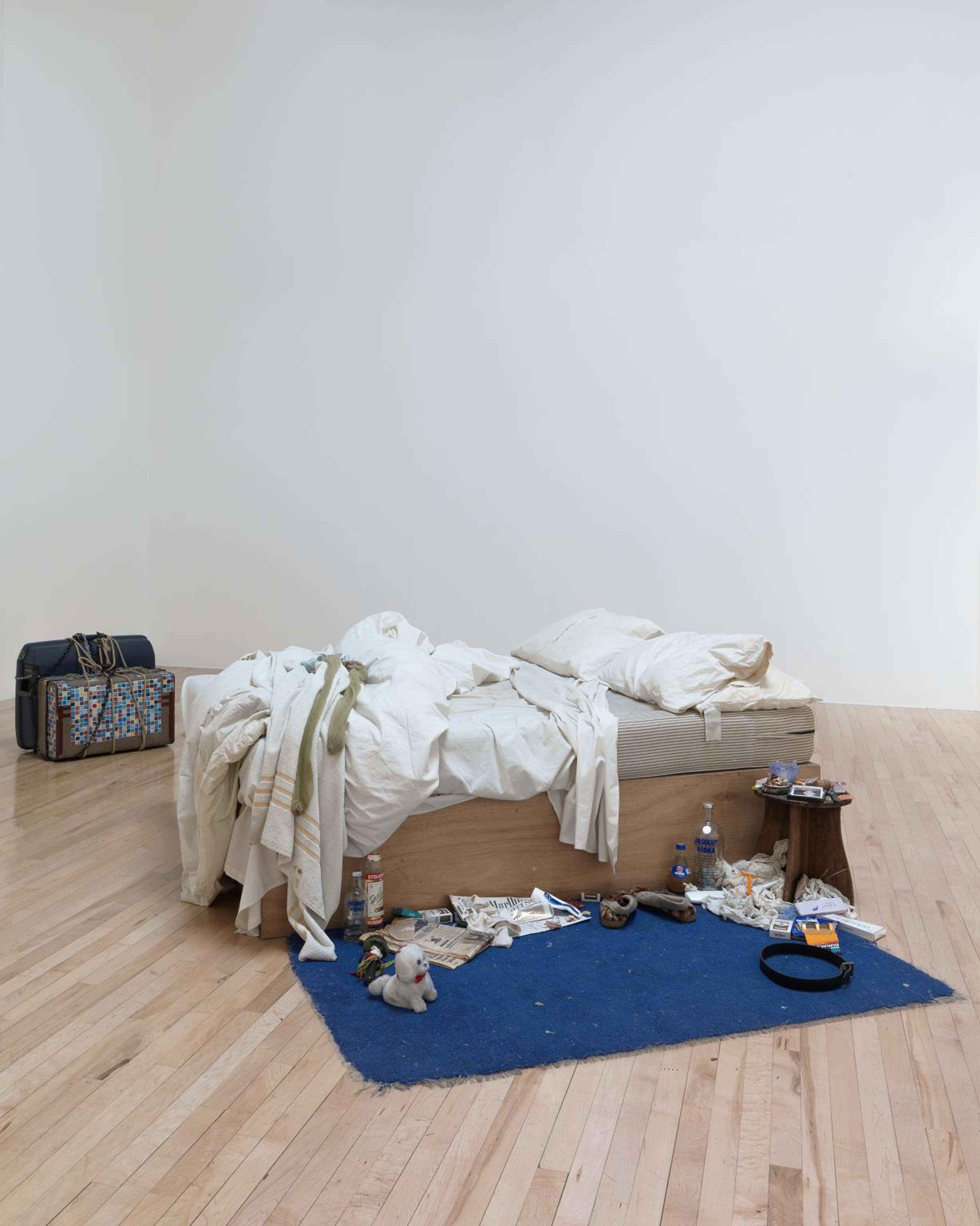 Une photographie de l'installation de Tracey Emin, "My Bed", représentant un lit défait avec des accessoires éparpillés dans la scène.
