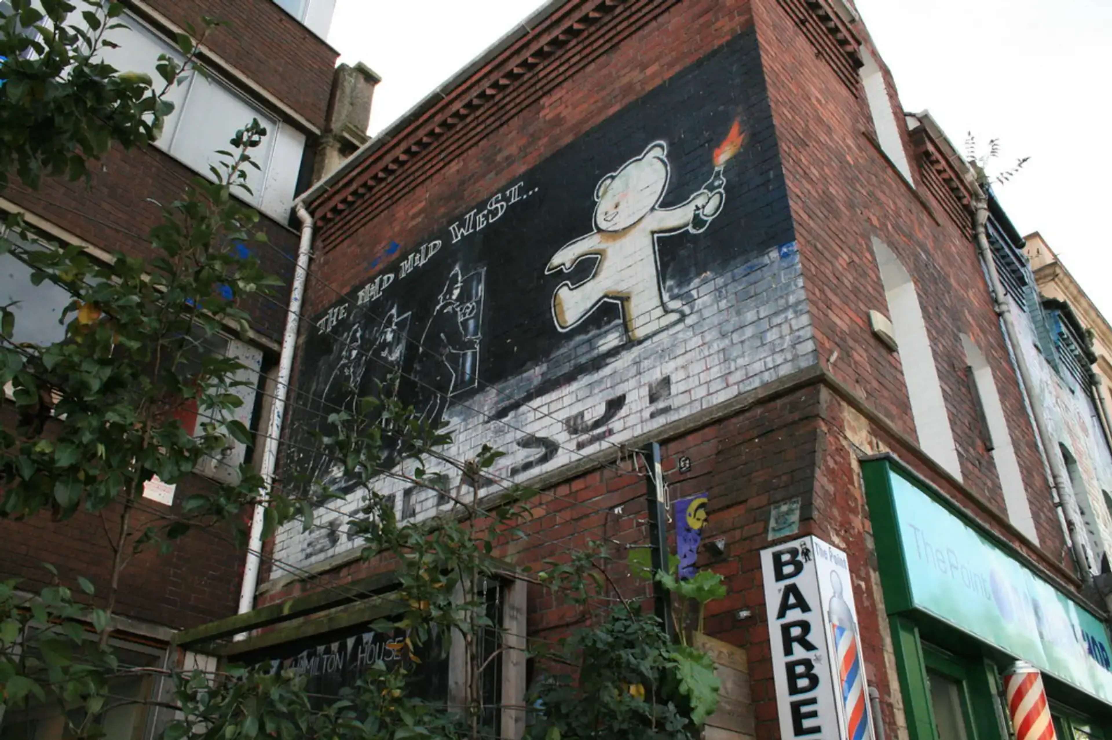 Photographie de l'œuvre murale originale de Banksy, « Mild Mild West », représentant un ours en peluche lançant un cocktail Molotov sur trois policiers anti-émeute.