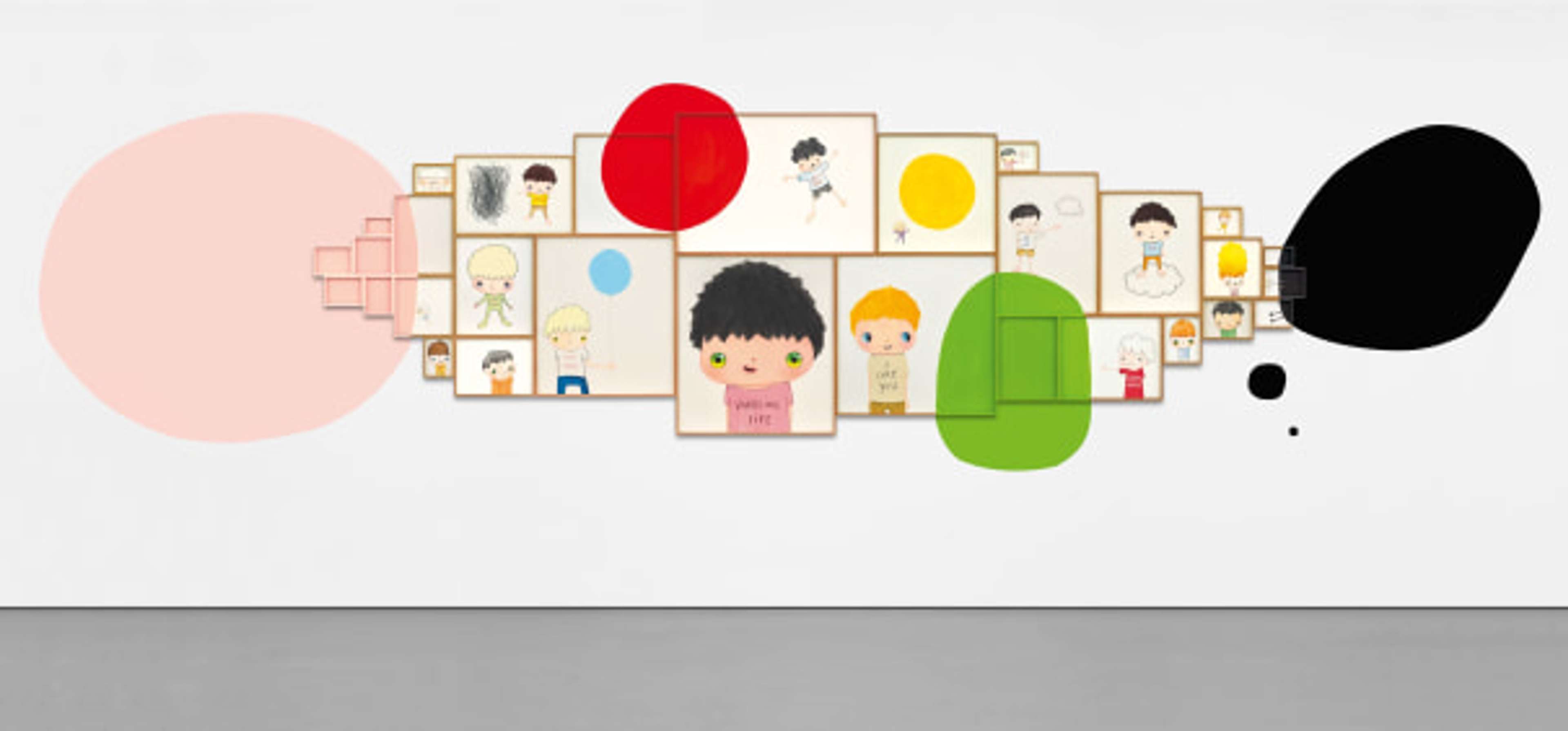 A large horizontal installation featuring thirty small, colourful drawings and painted shapes arranged in a playful sequence across a white wall, with recurring cartoon faces overlaid with colourful ‘blobs.’