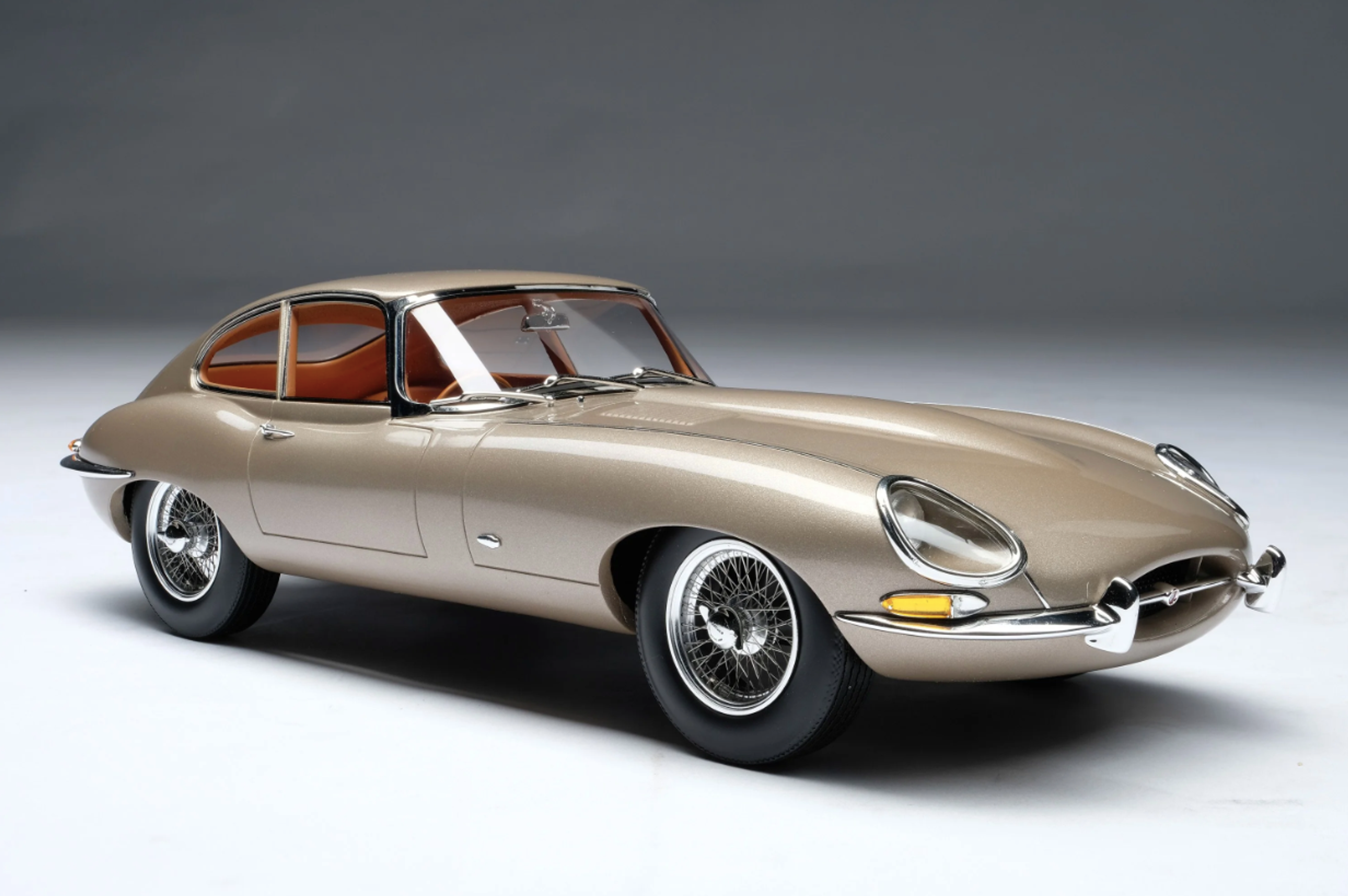 Une Jaguar E-type Coupé de couleur champagne de 196x, sur un fond de studio uni.