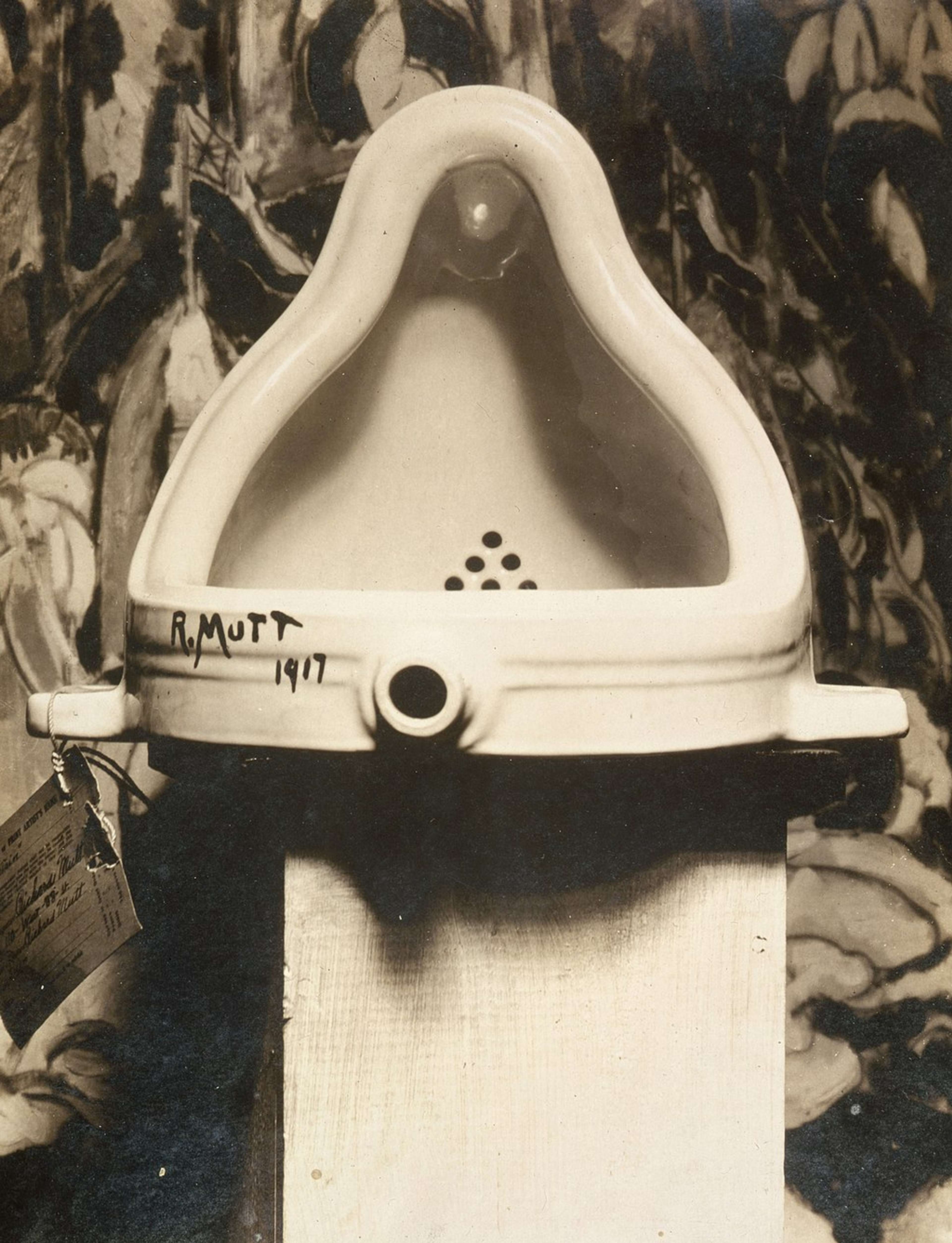 Une image de l'urinoir qui est devenu *Fontaine* de Marcel Duchamp. C'est un urinoir blanc, avec la signature R. Mutt 1917 dans le coin inférieur gauche.