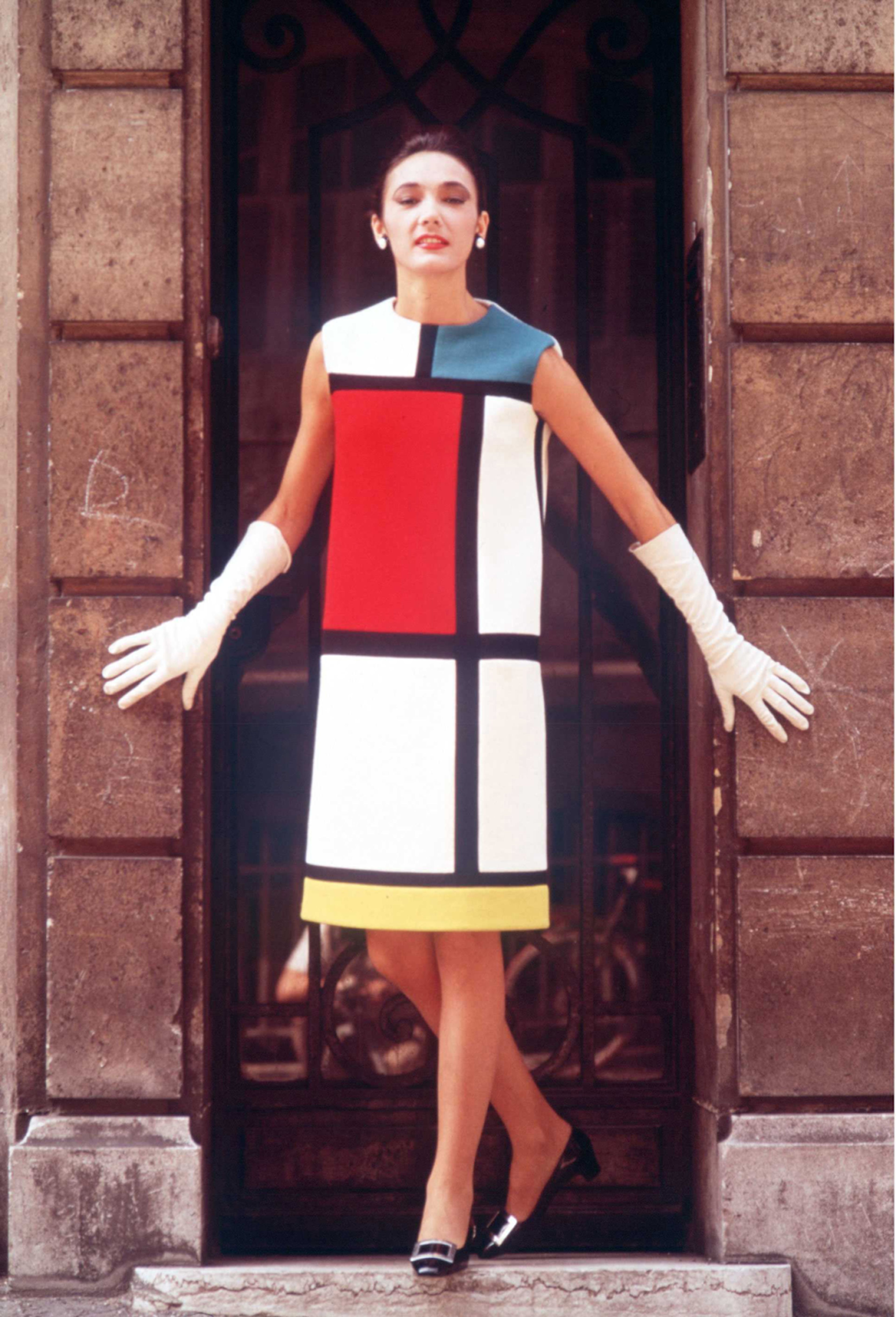 Une femme se tenait dans une embrasure de porte, vêtue d'une robe de cocktail ornée de rectangles graphiques blancs, rouges, jaunes et bleus, délimités par de épaisses lignes noires.