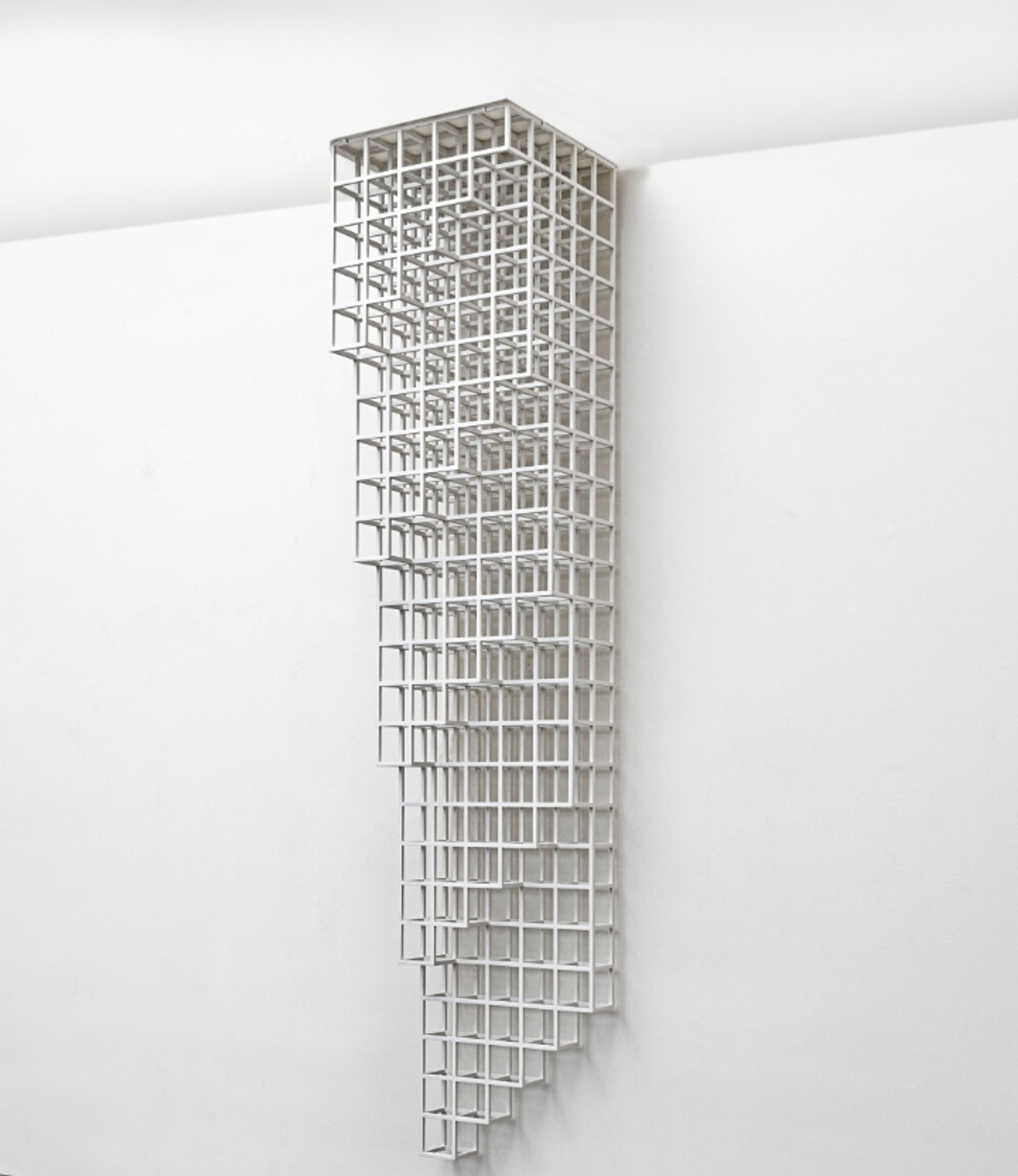 A geometric arrangement of open cubes that appear to be hanging from a square horizontal plate. The planes of cubes are the longest at the point where the structure attaches to the white wall behind it, getting shorter as they extend out into the room, with a slanted edge.