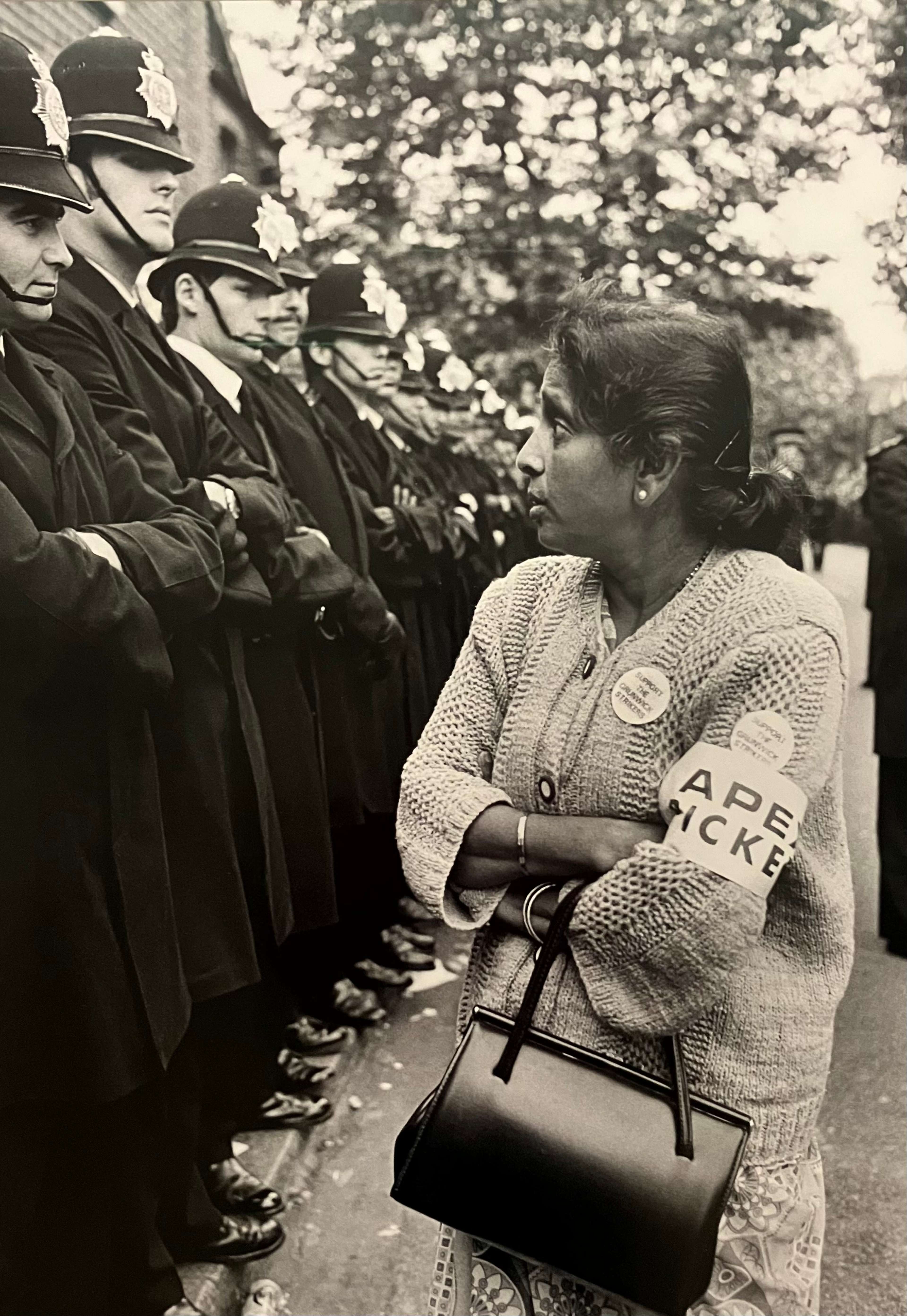 Une femme se tient avec défi devant une rangée de policiers.
