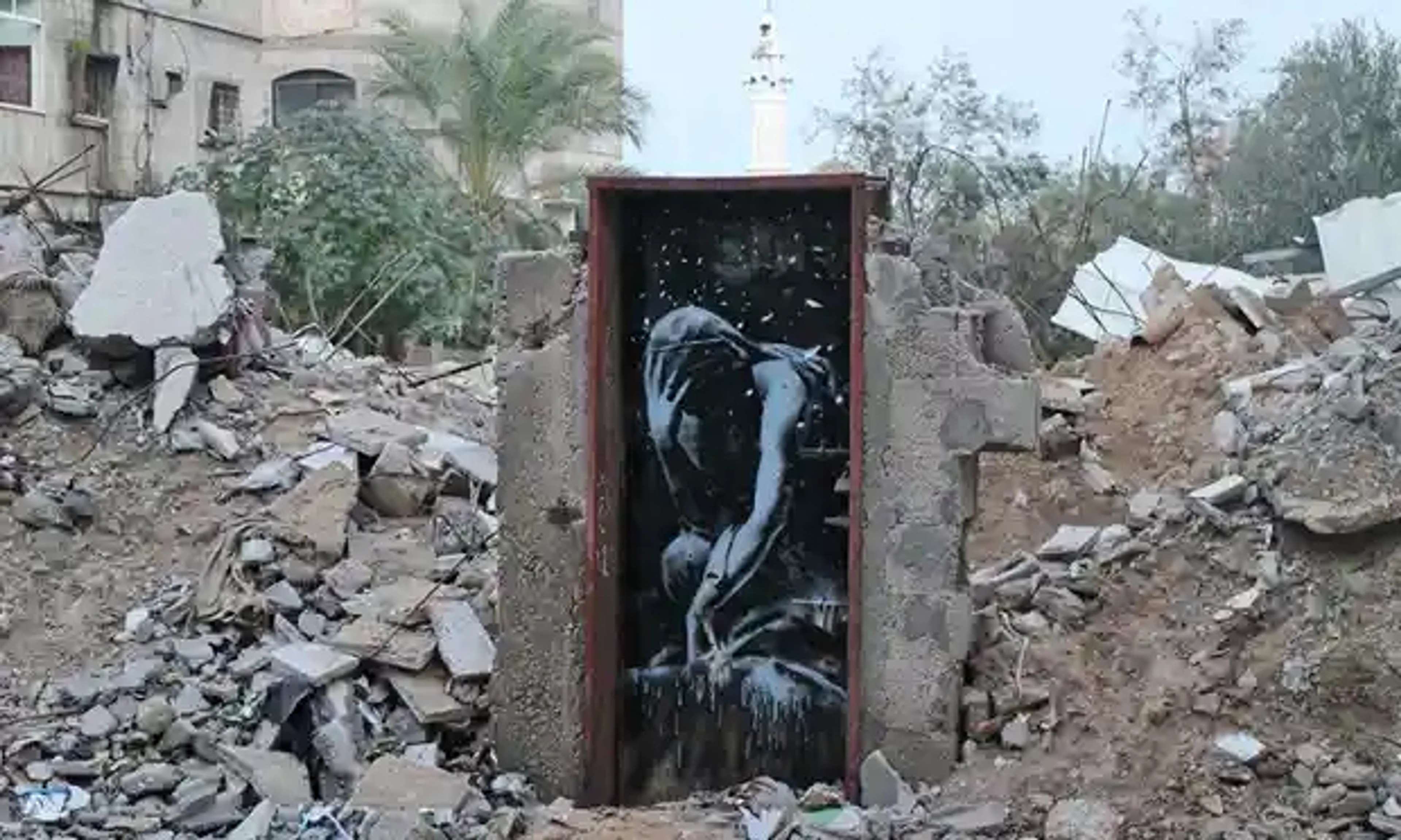 Une image d'une fresque murale de Banksy au milieu des décombres à Gaza. Elle représente un homme penché, la tête dans les mains, représenté en monochrome. L'œuvre est intitulée "The Man".