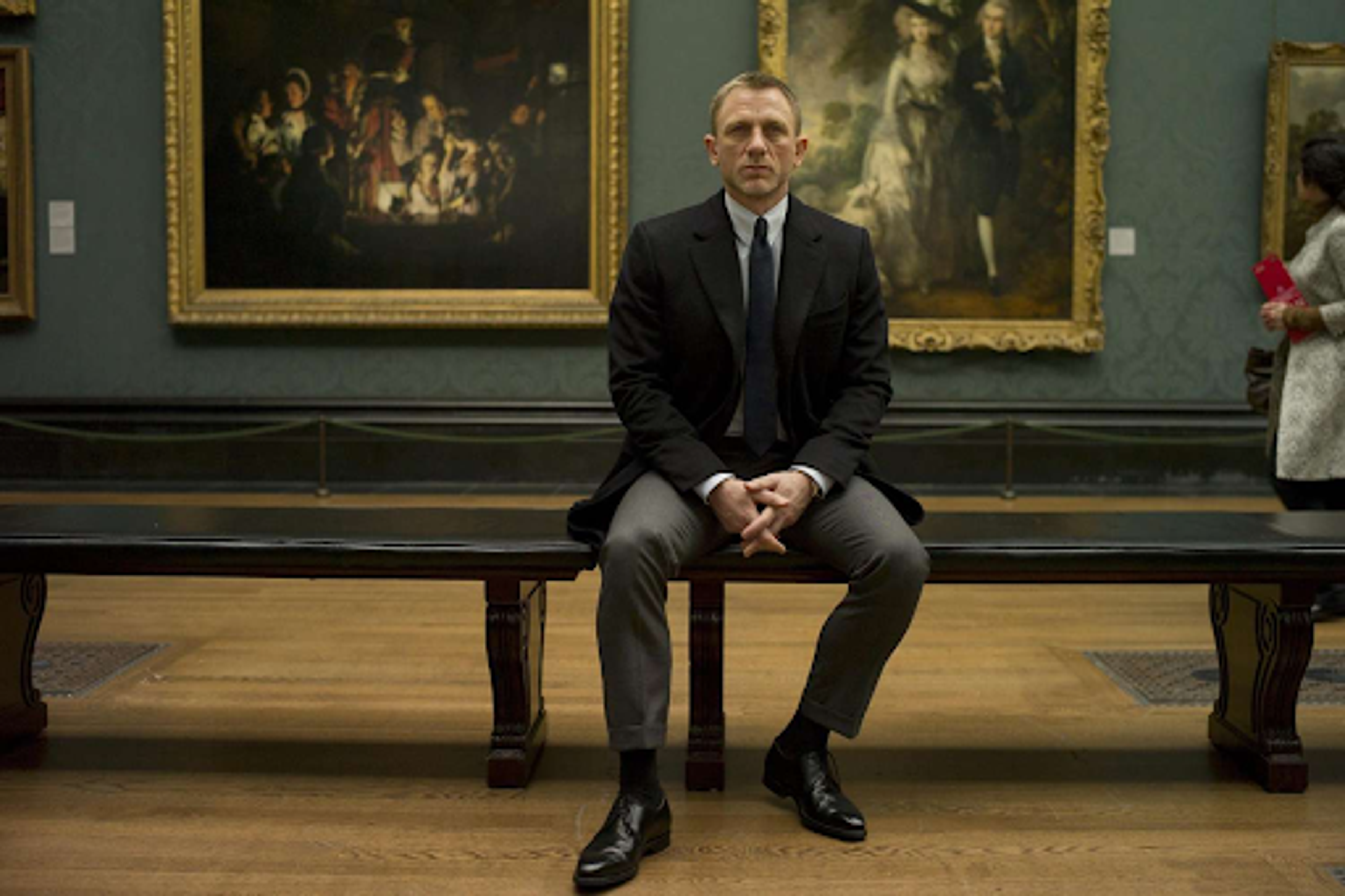 Photographie tirée du film Skyfall. Un homme est assis sur un banc à l'intérieur d'une galerie d'art.