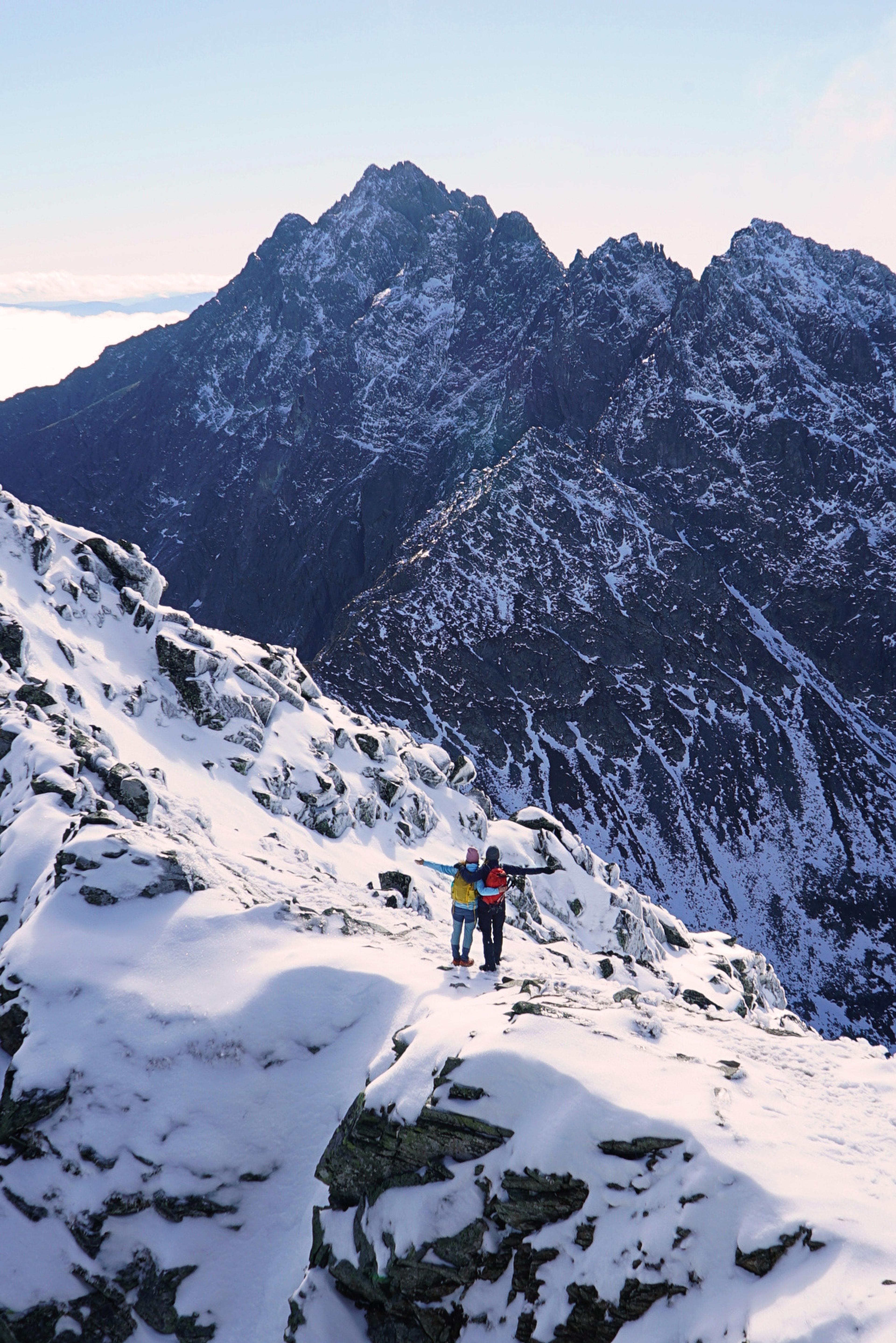 Two figures on a snow-dusted summit ridge in the High Tatras, jagged peaks behind