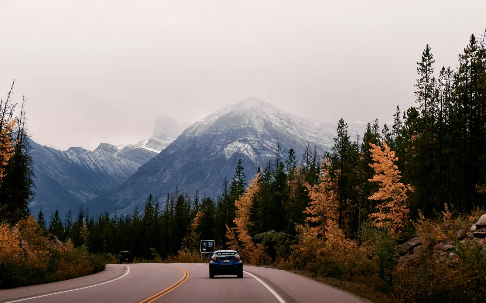 A car travelling the Icefields Parkway with Rocky Mountain peaks behind it