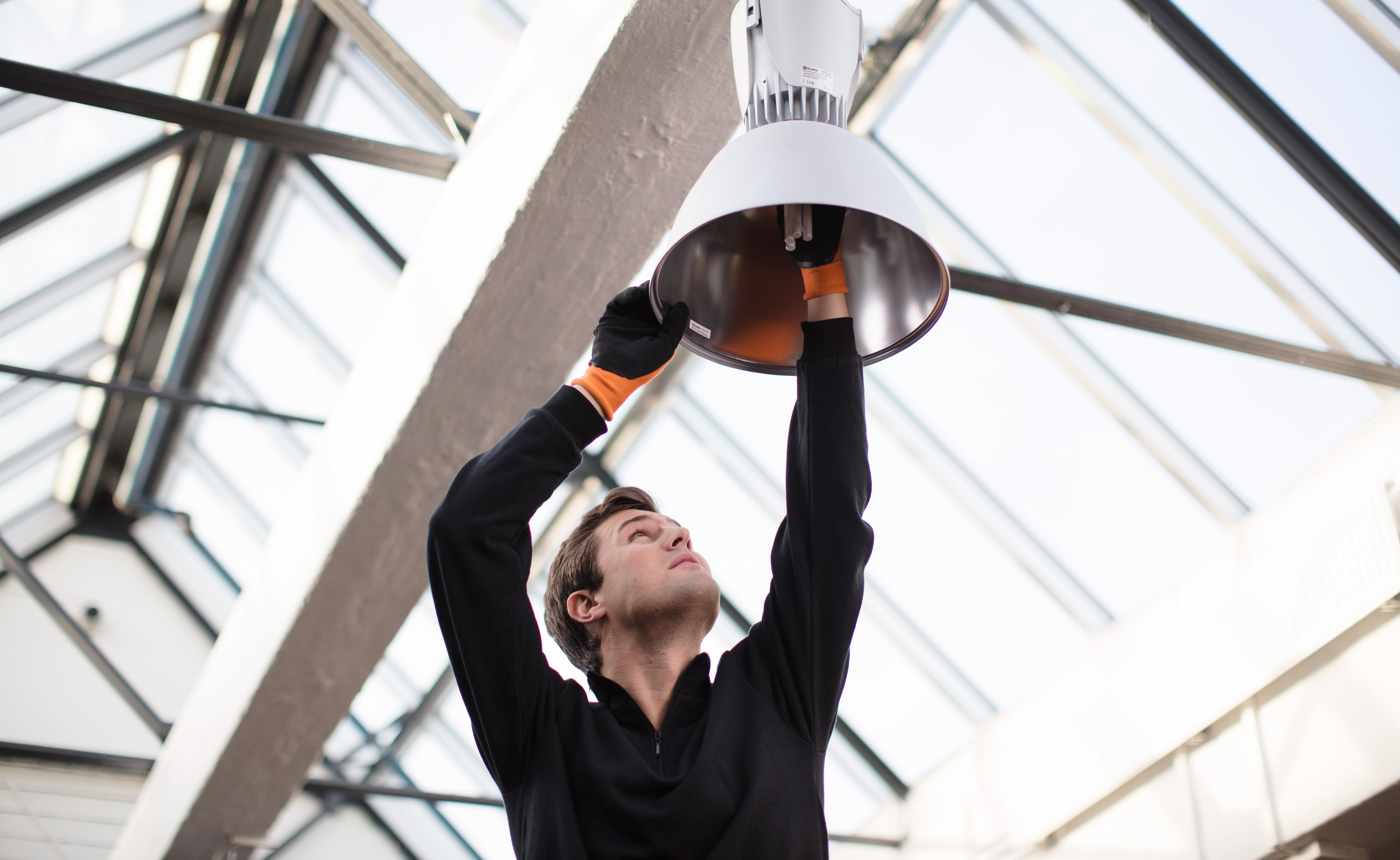 Bilde av mann fra Eir som skifter lyspære i en lampe høyt under taket