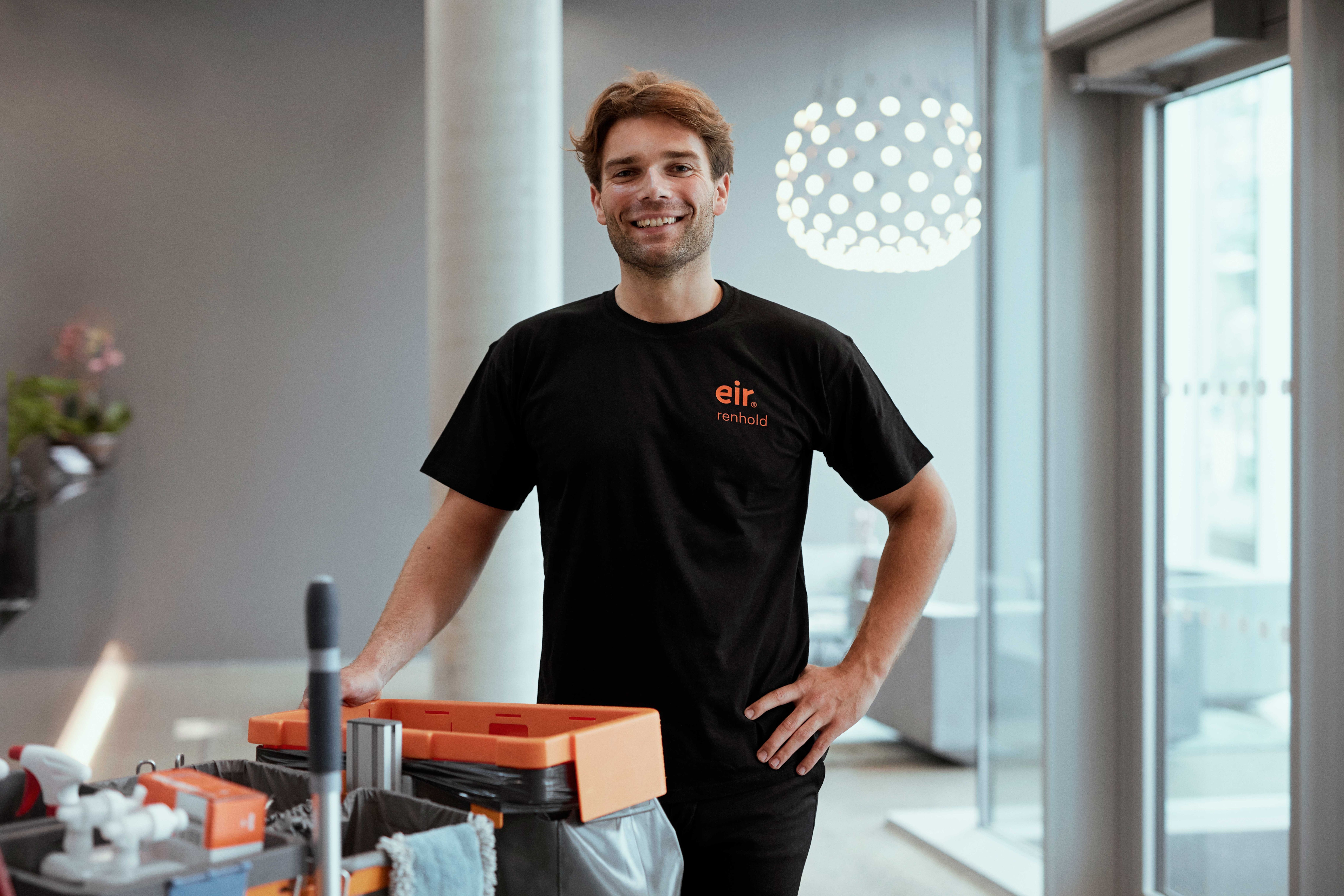 Foto av mann i Eir-uniform i et lyst lokale smiler til kamera