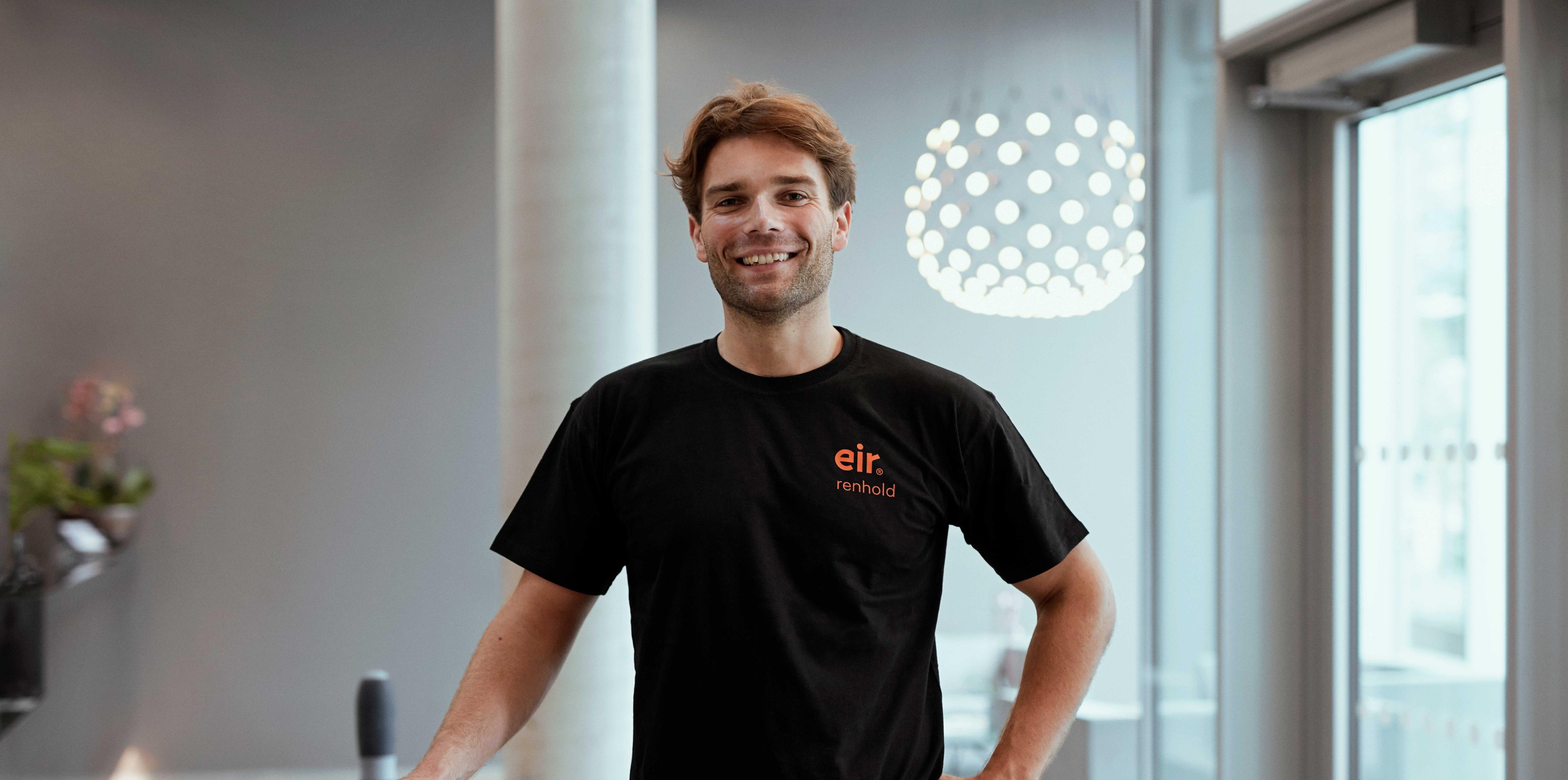 Foto av mann i Eir-uniform i et lyst lokale smiler til kamera