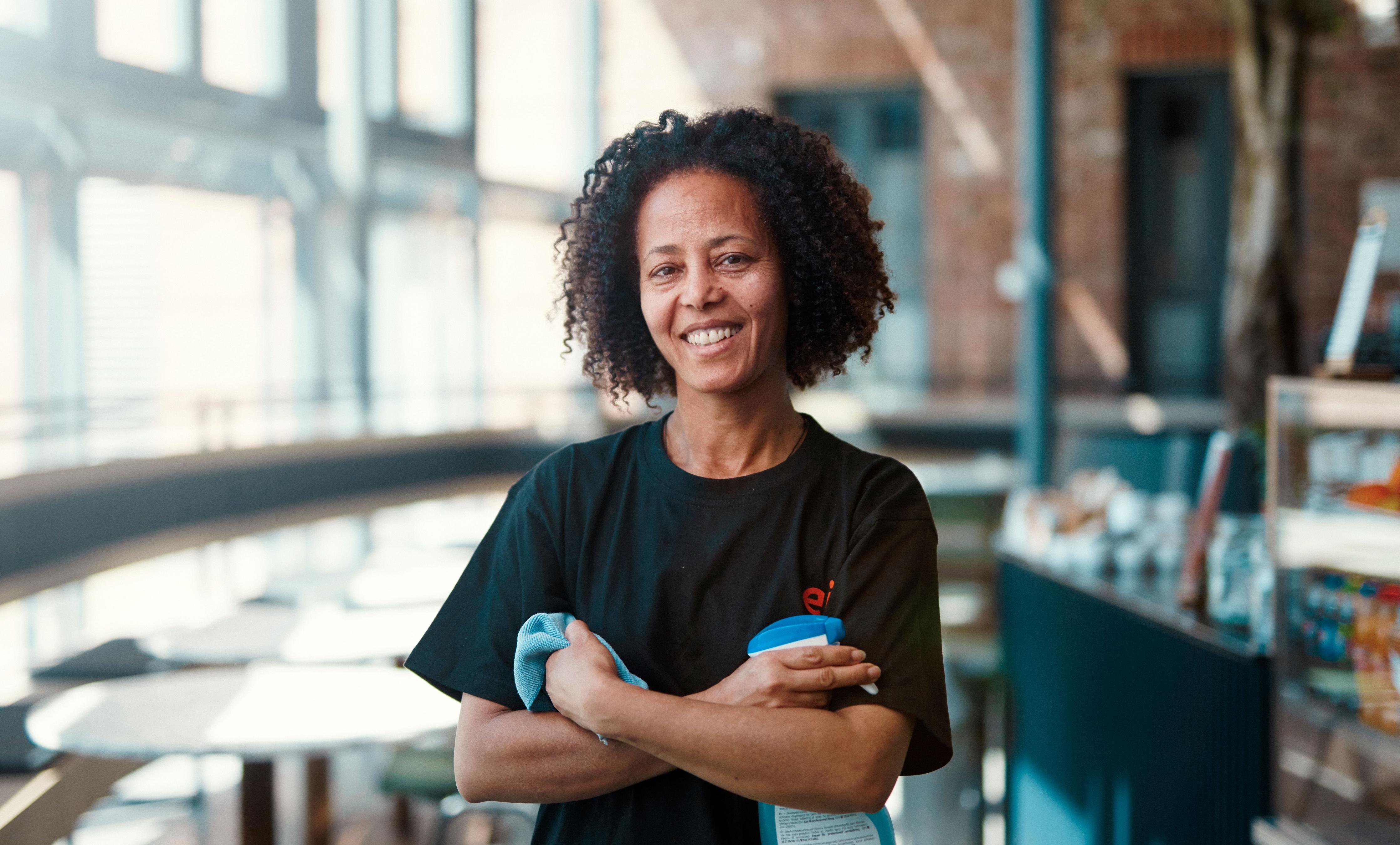 Bilde av dame fra Eir smiler med hendene i kryss. Hun har en klut i ene armen, og en sprayflaske med rengjøringsmiddel i den andre hånden