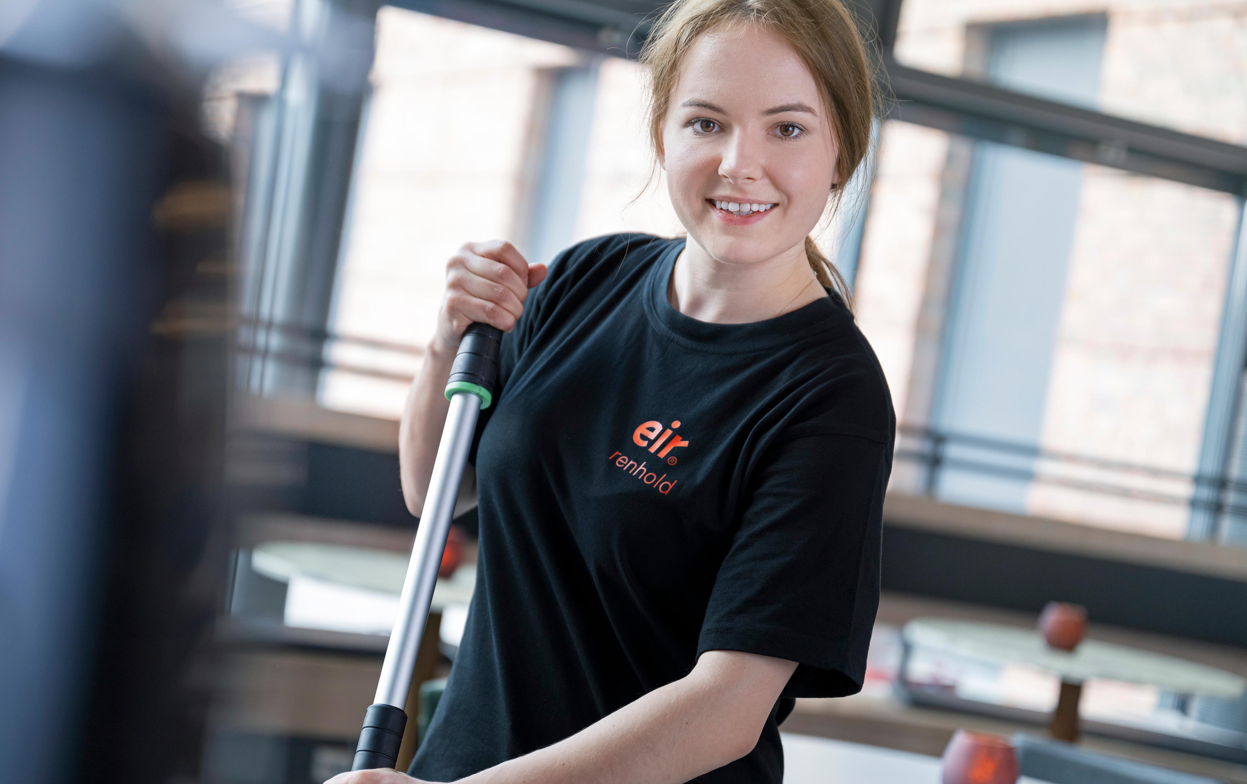 Foto av dame og mann i Eir-uniform står sammen i en kantine. Damen holder en i vasketralle og mannen holder en gulvmopp
