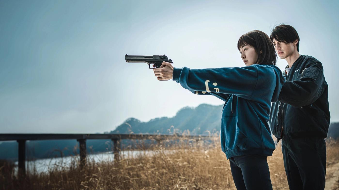 Jeong Ji-an berlatih menembak dengan pistol sementara didampingi seorang pria di lapangan terbuka