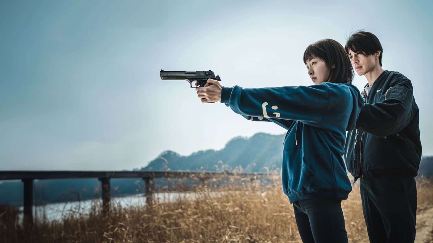 Jeong Ji-an berlatih menembak dengan pistol sementara didampingi seorang pria di lapangan terbuka
