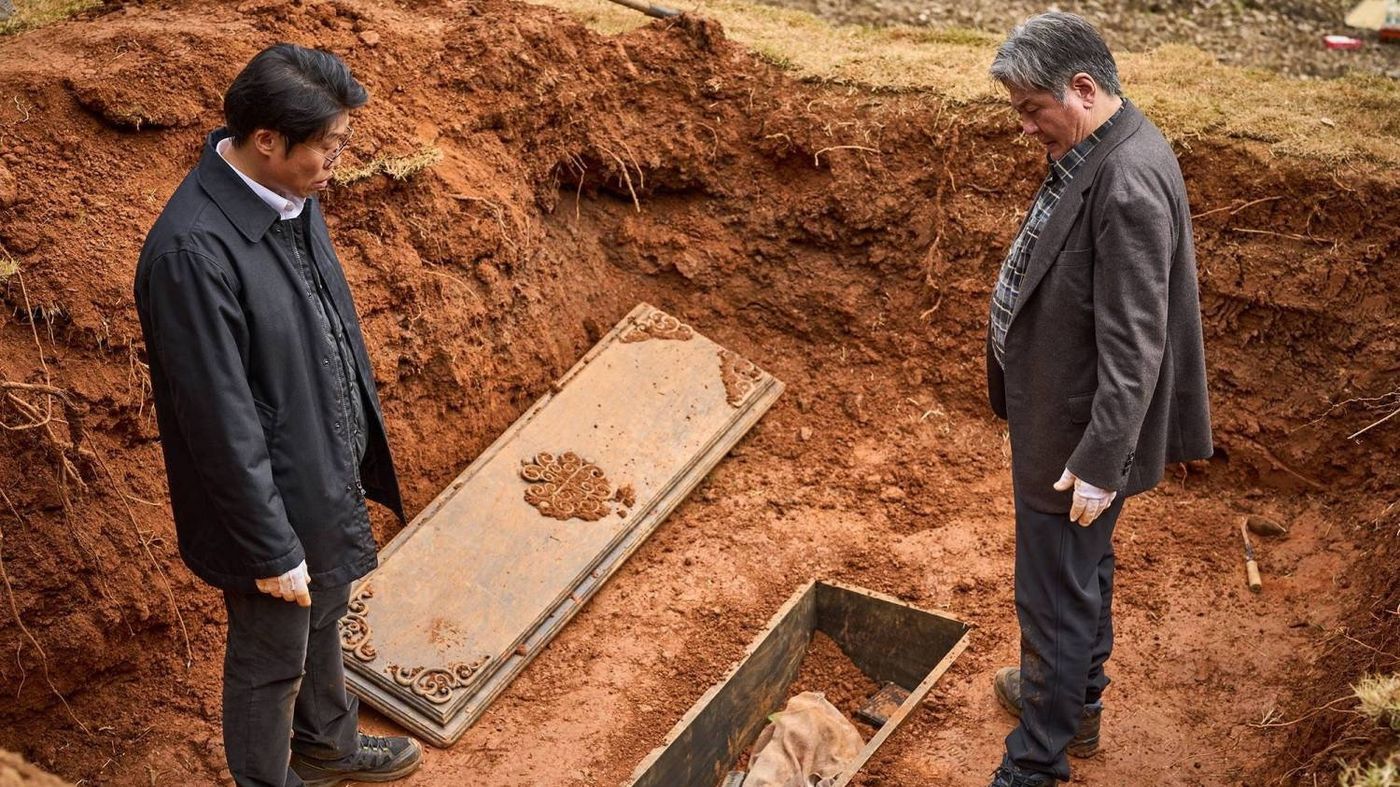 Dua karakter membuka tutup peti mati kuno yang baru digali dalam adegan Exhuma