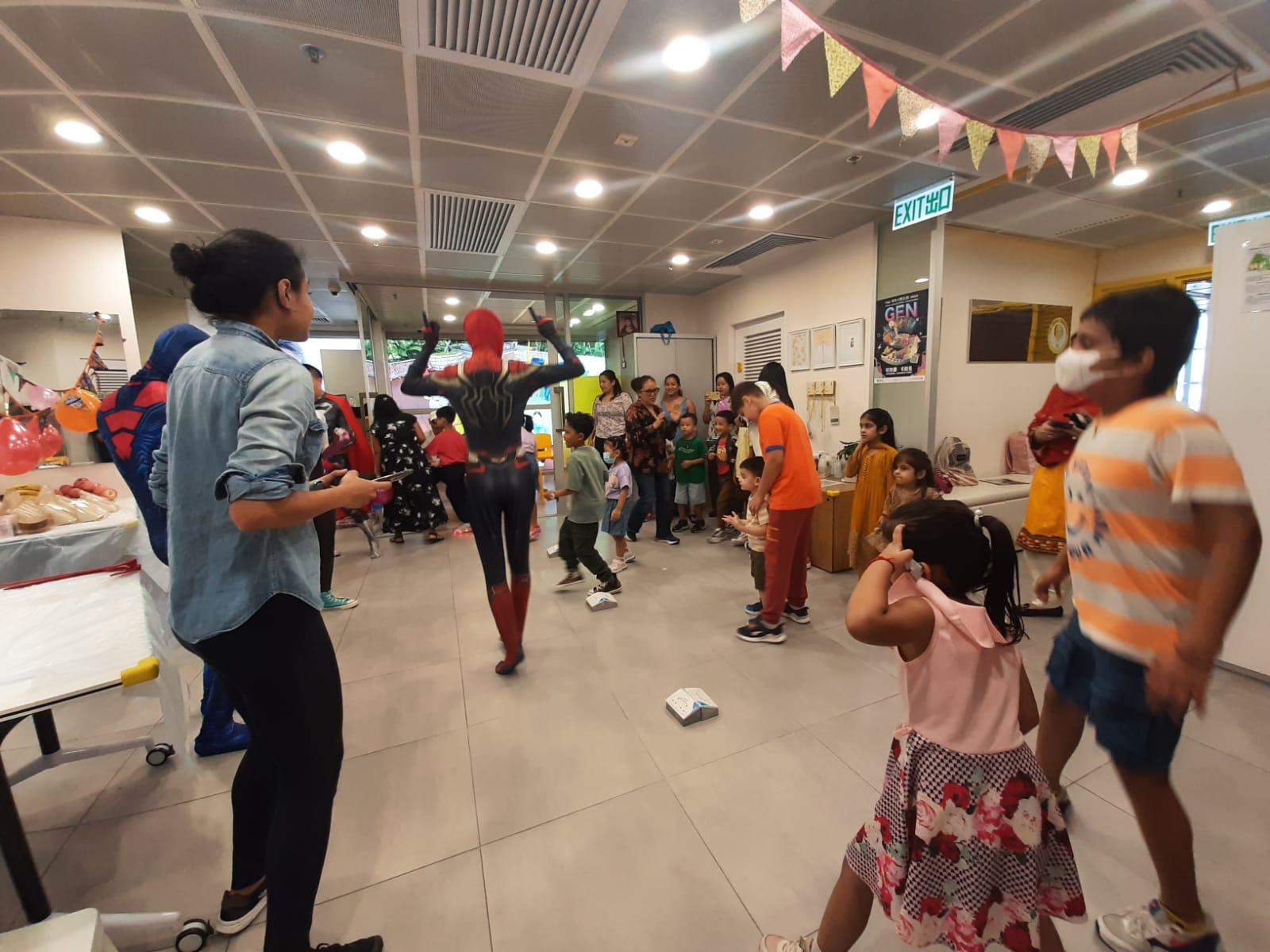 Adults and children stand around the room during a group game.