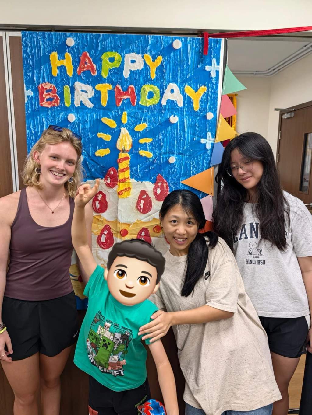 A child and volunteers pose beside a handmade birthday backdrop.