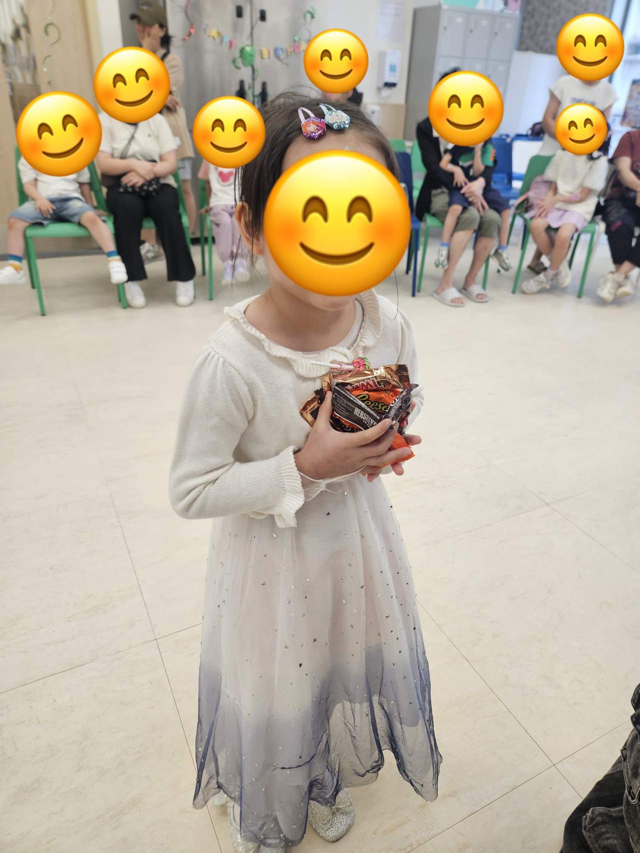 A child stands holding a small ball before a seated group.