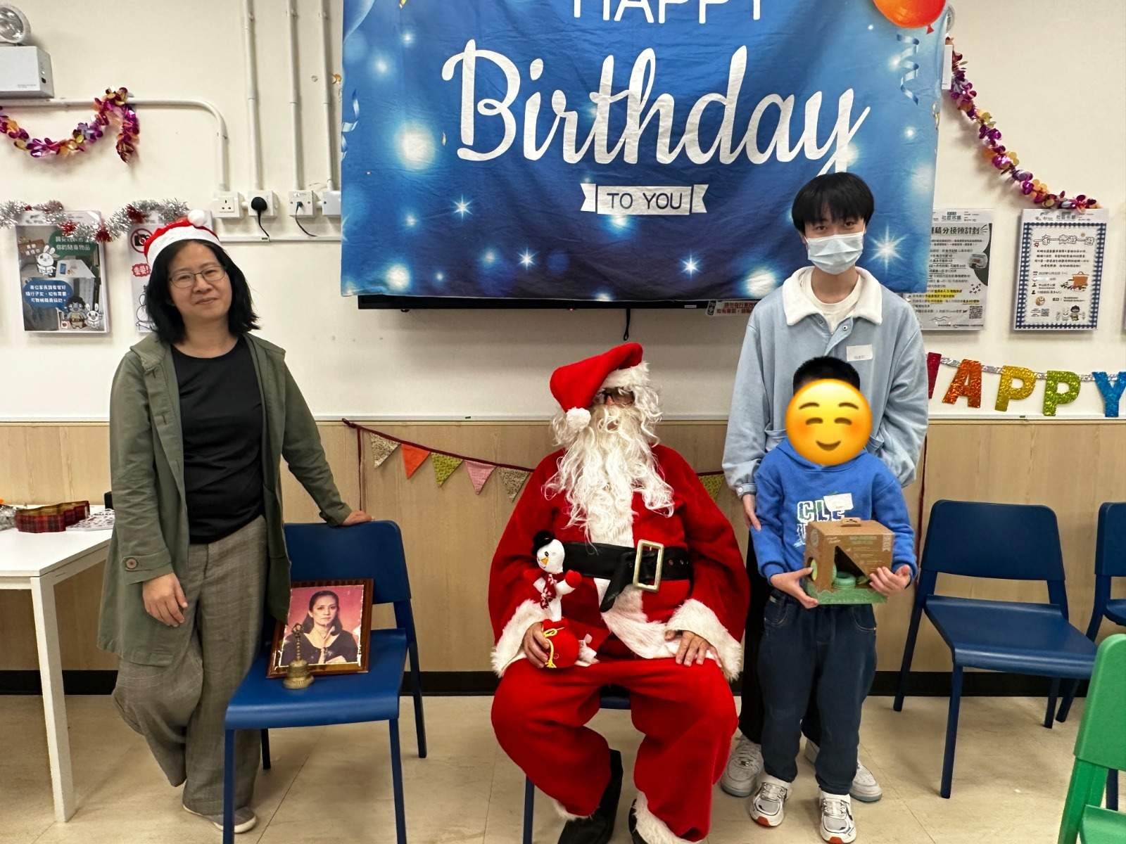 A costumed adult sits between an adult and child holding gifts.