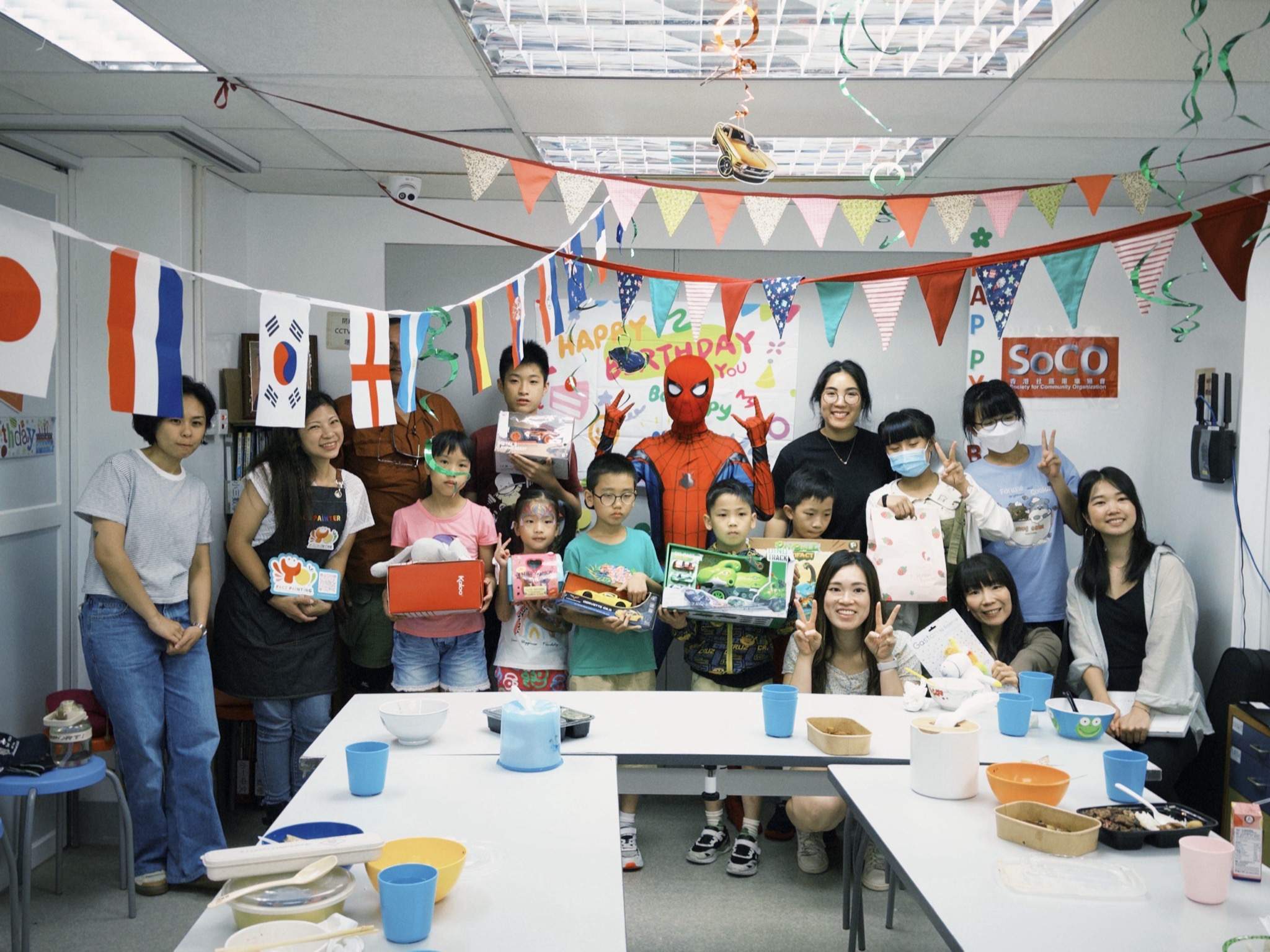 A large group poses behind tables beneath colourful flags.