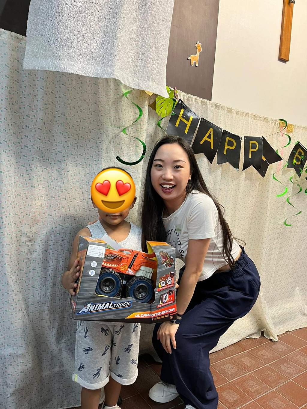 An adult kneels beside a child holding a boxed toy.