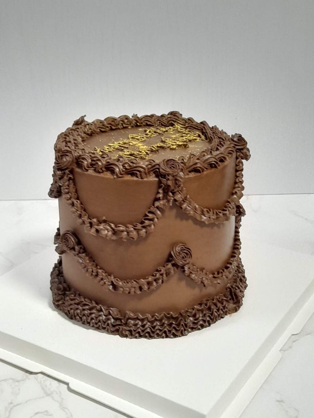 A vintage-style chocolate cake with piped frills and gold lettering, by Bakelicious By Aisha.