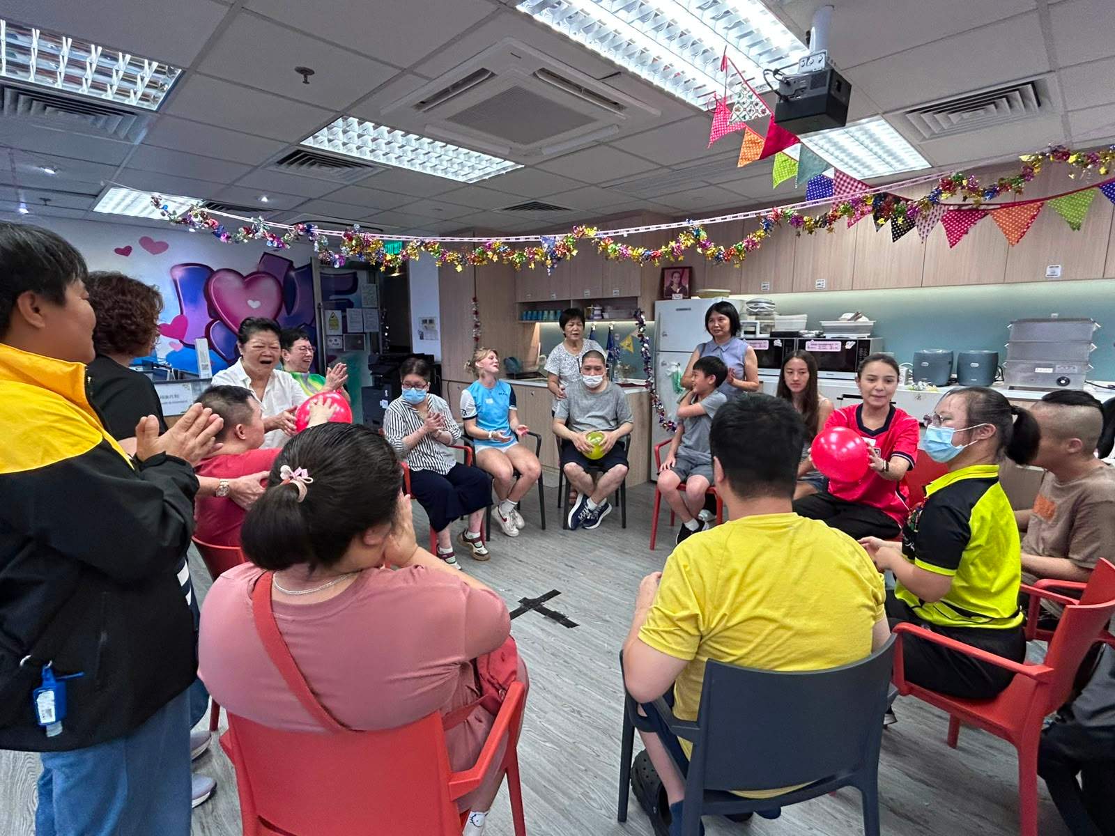 A large group sits in a circle beneath hanging decorations.