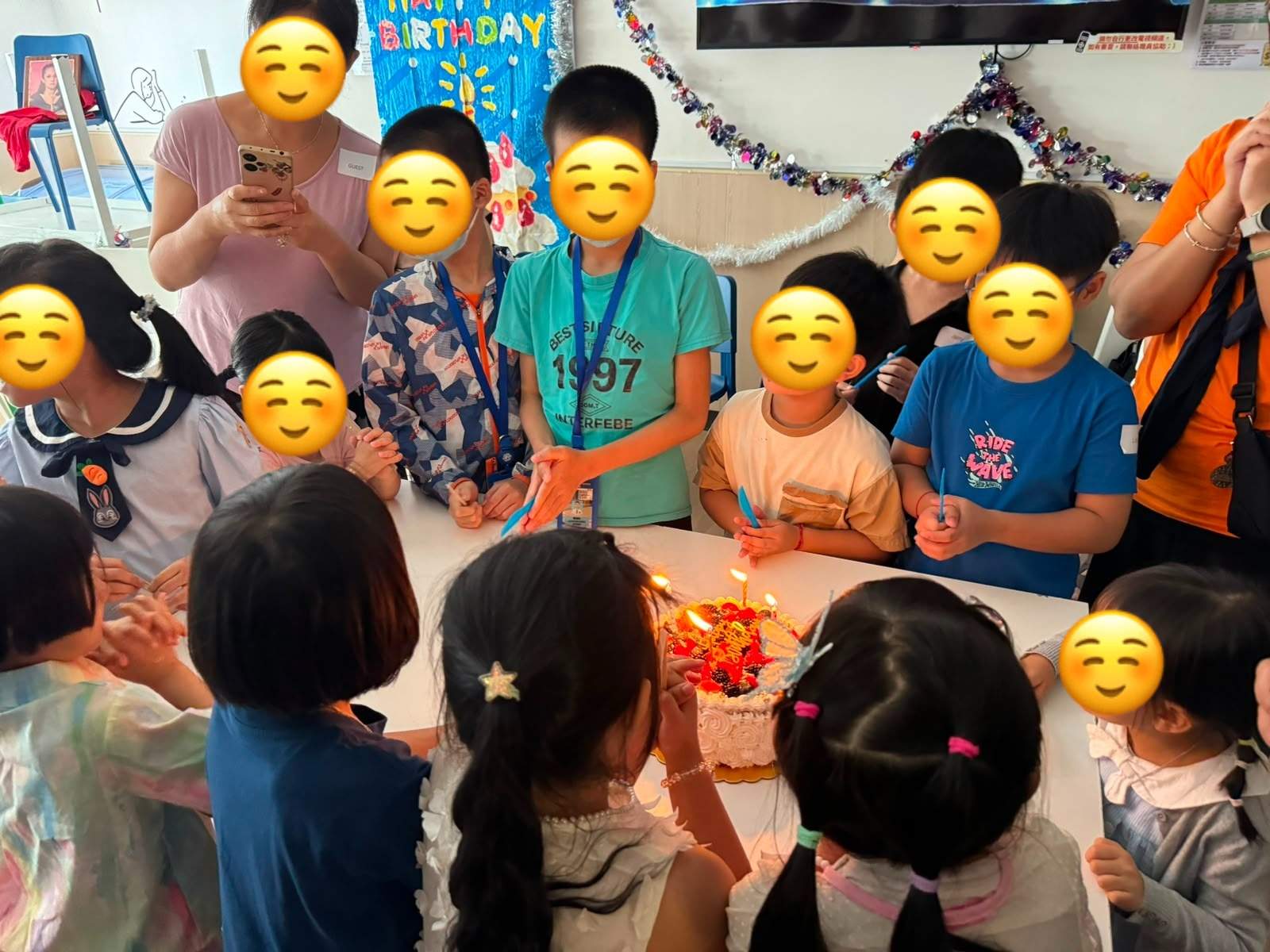 Children gather around a candlelit birthday cake.