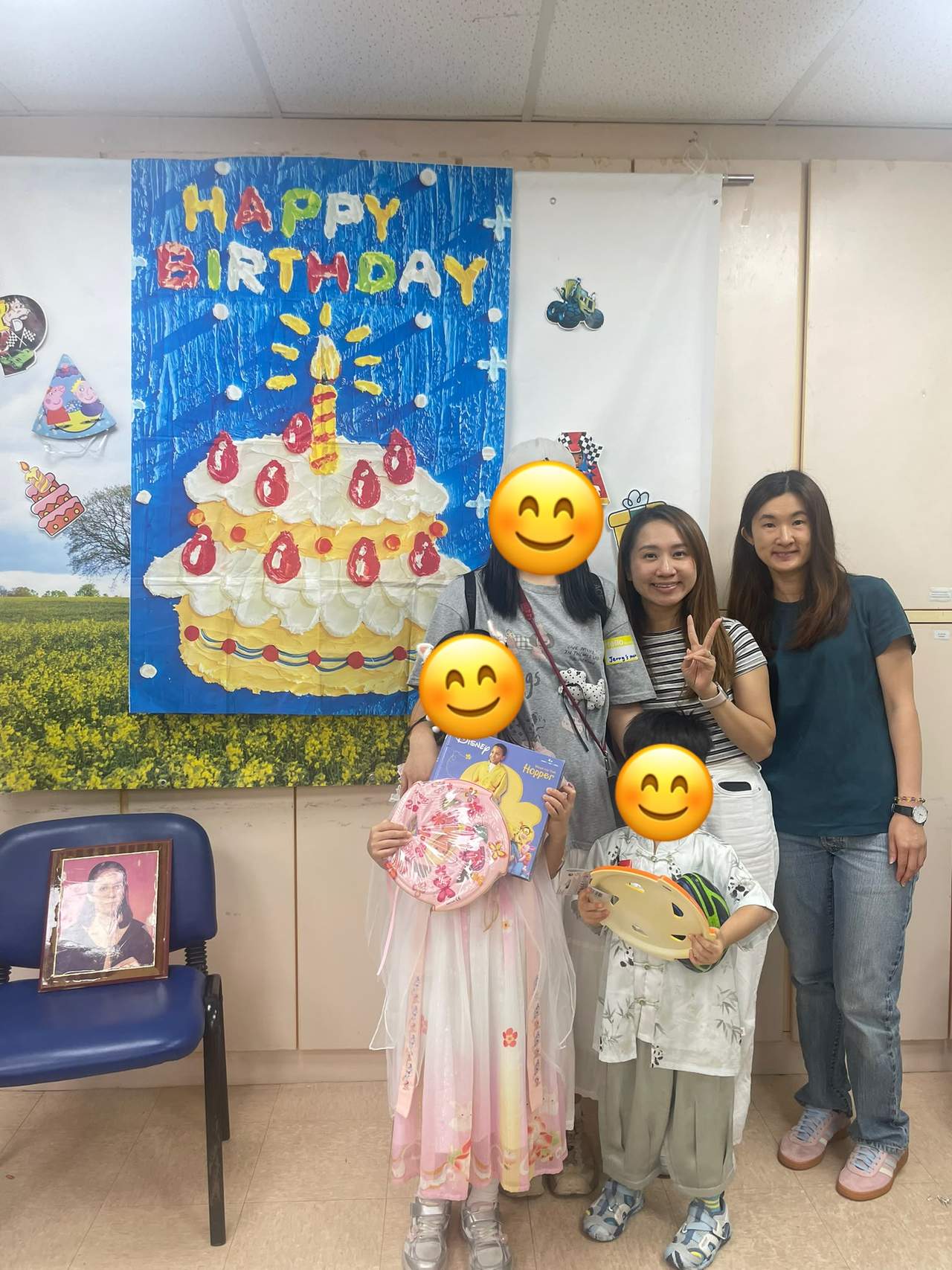 Children hold gifts while posing with adults before birthday decorations.