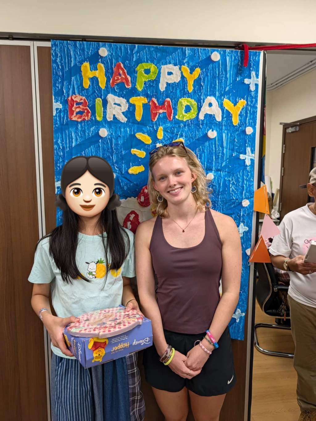 A child and volunteer pose with a gift beside the backdrop.