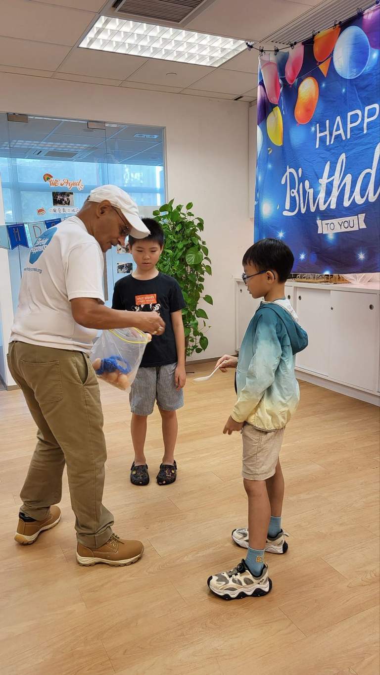 An adult presents an item to a child near the backdrop.