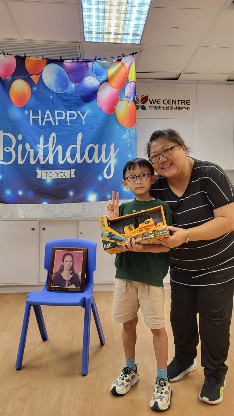An adult and child hold a cake beside a framed photograph.