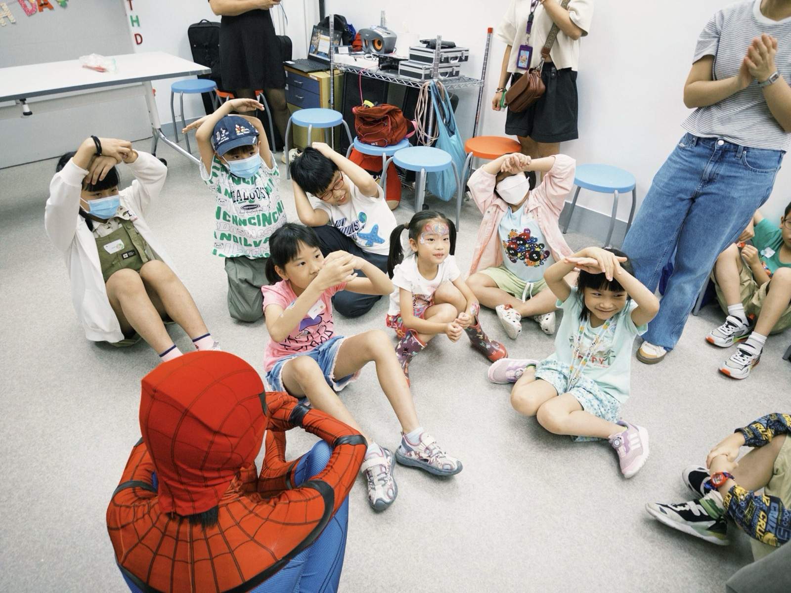 Children copy gestures while seated around a costumed performer.