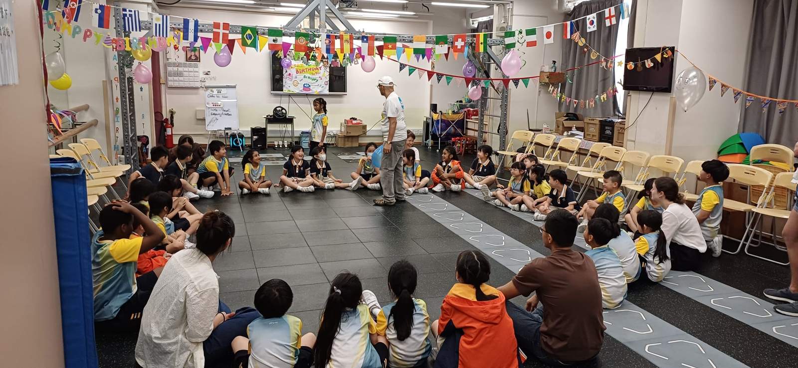 Children and adults sit in a large circle around the room.