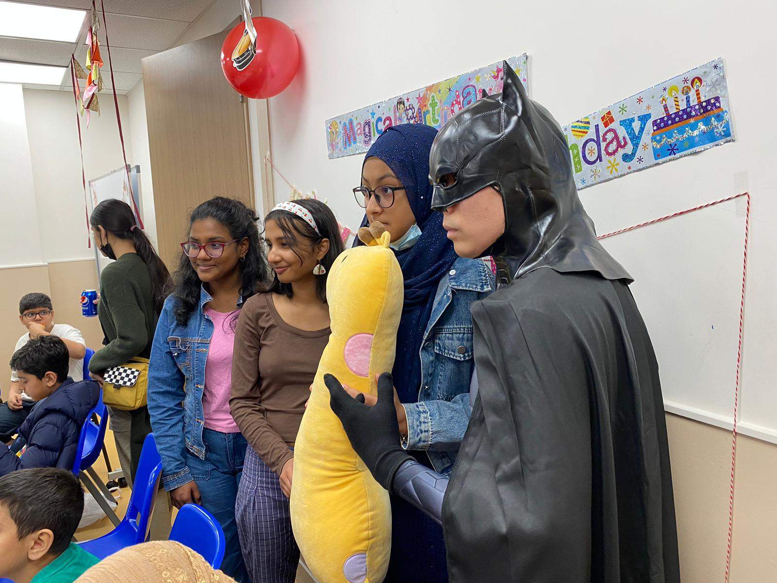 Adults and children pose beside a dark-caped costumed performer.