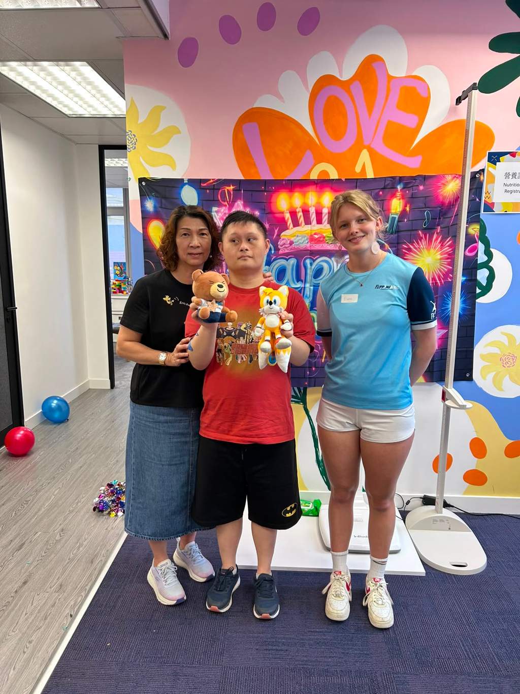 Three people pose together while displaying several stuffed toys.