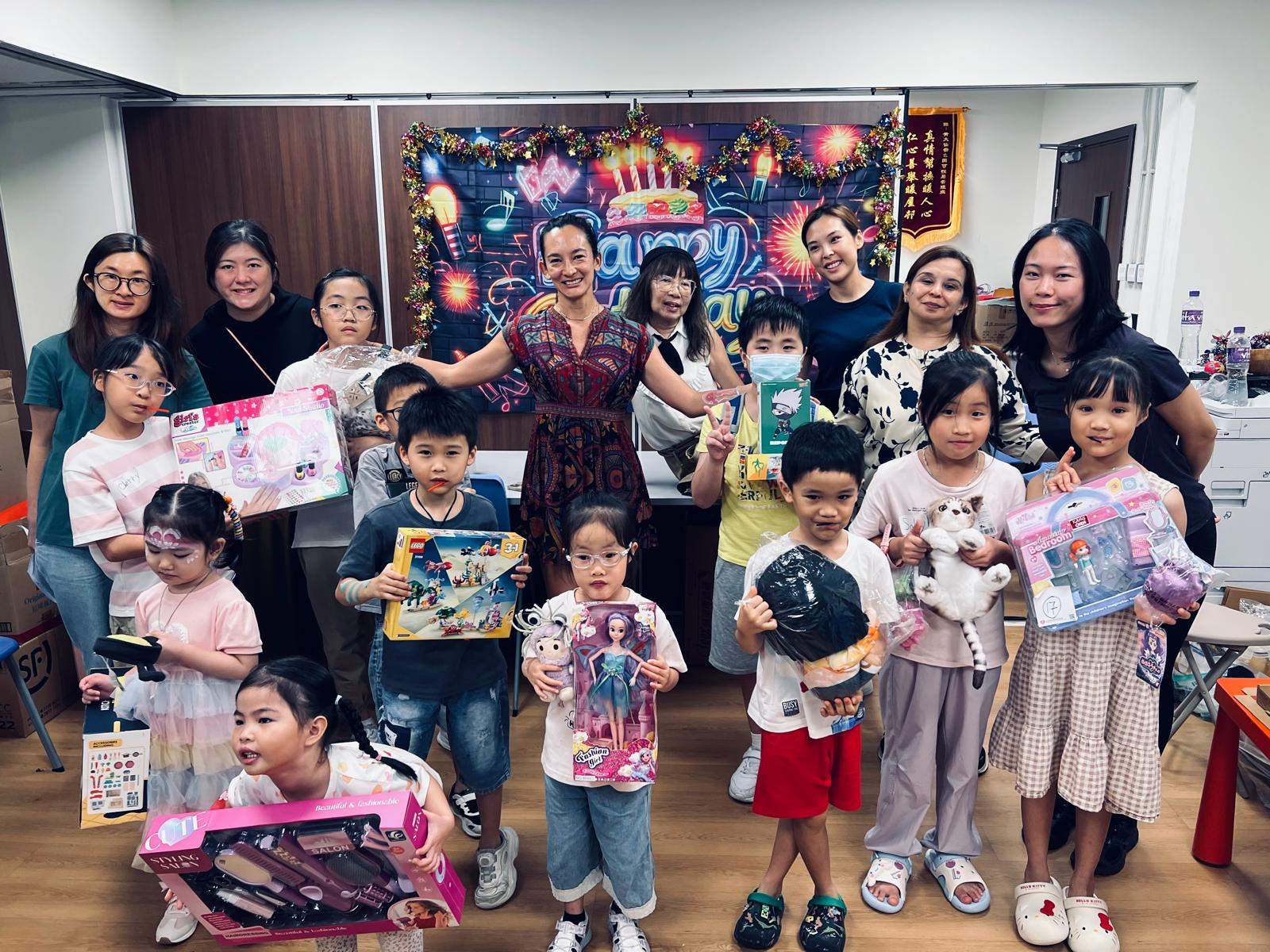 Children and adults pose together while holding boxed gifts.